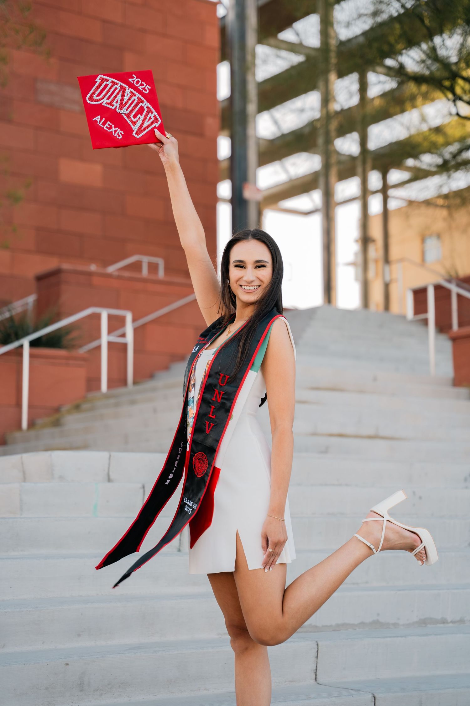 Graduate strikes playful poses on concrete steps during UNLV campus graduation photoshoot.