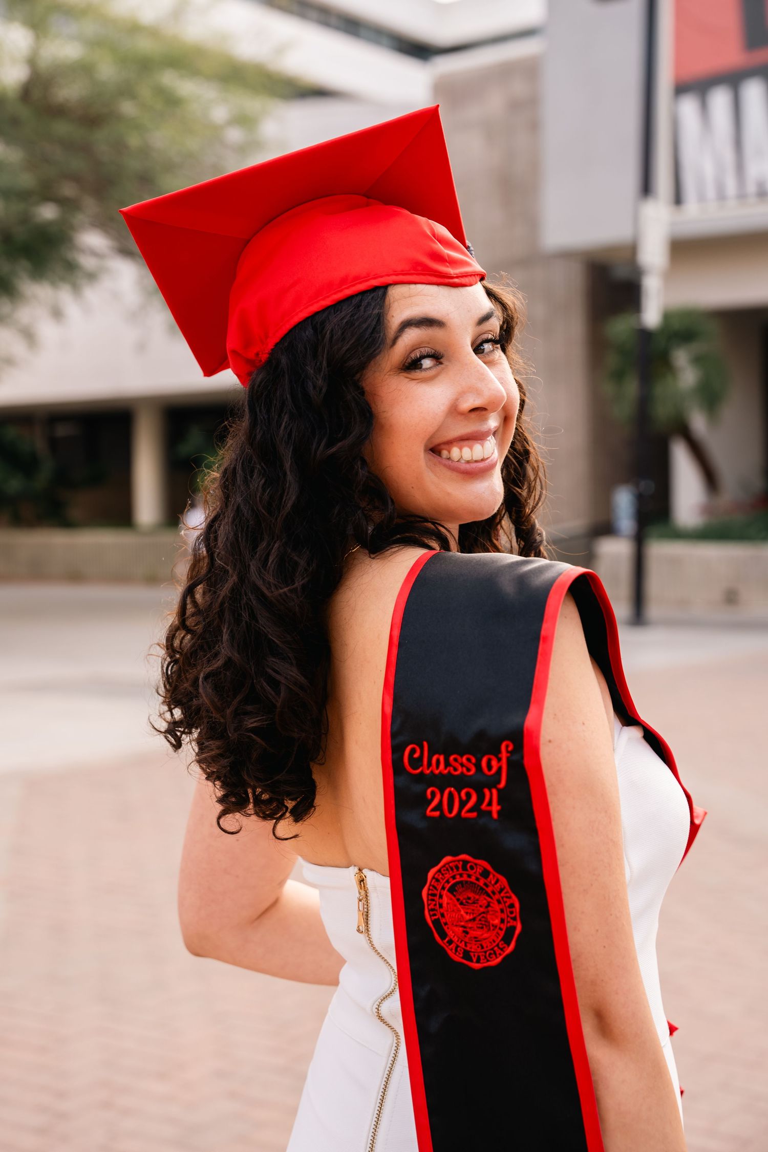 Graduate in red cap and white dress shows off Class of 2024 graduation sash.