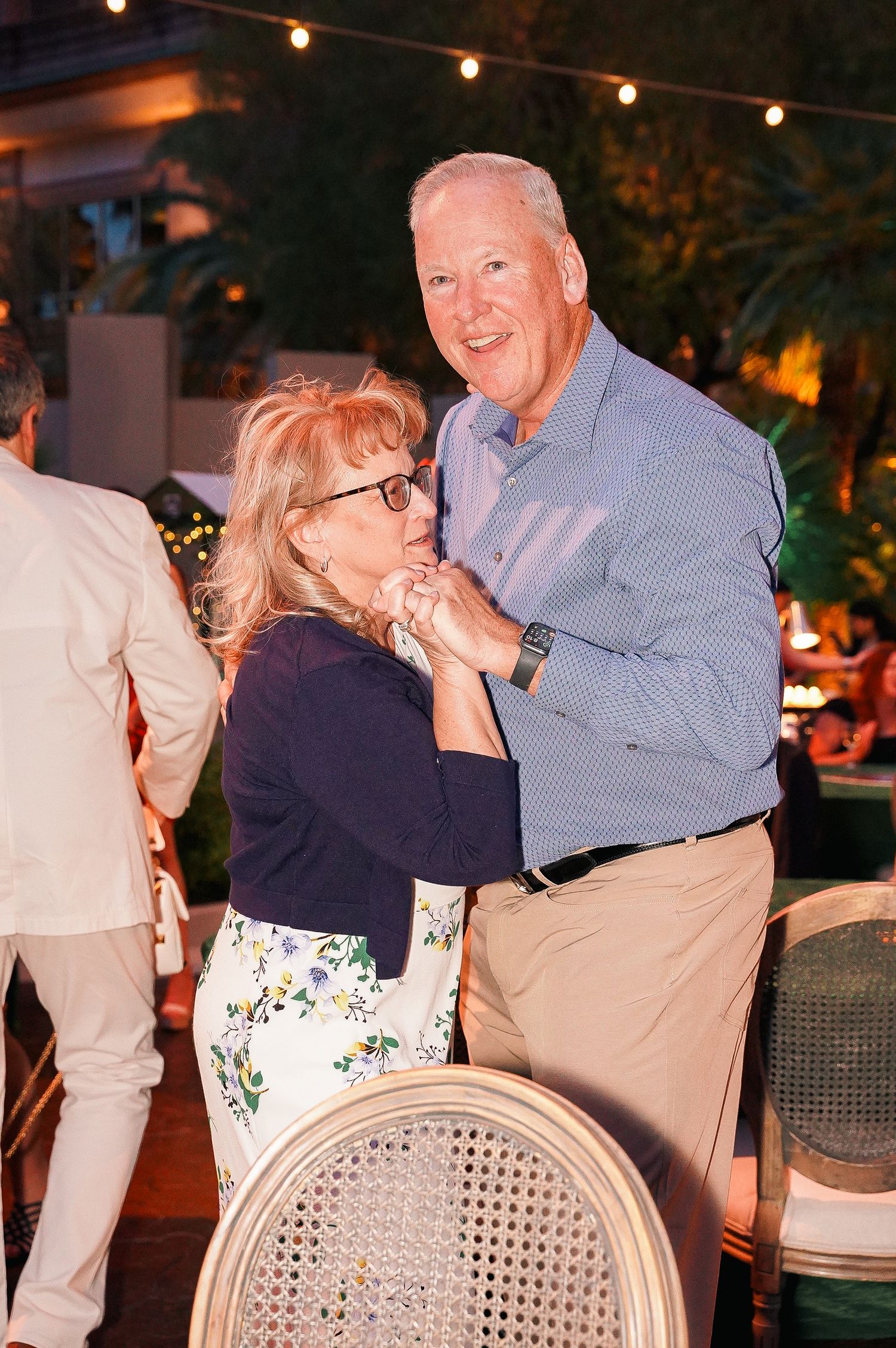 A couple dancing together at an evening outdoor party with string lights in the background.