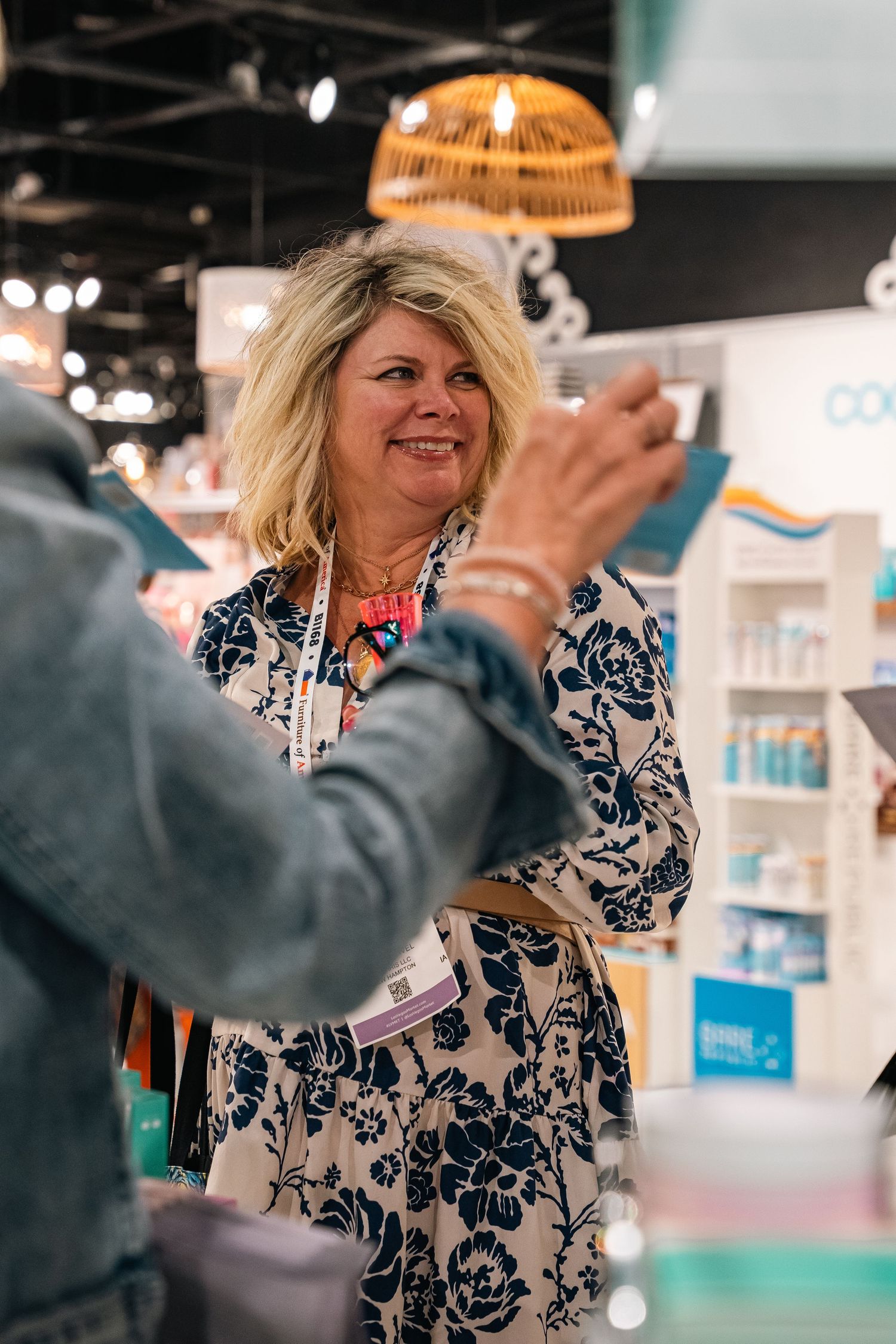 Woman in floral dress engaging with others at retail store event.