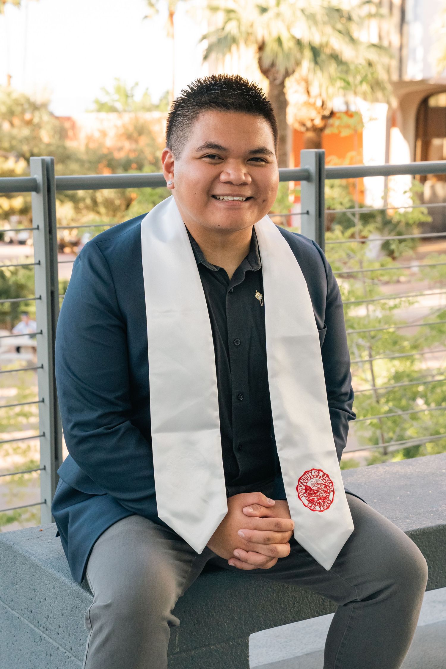 Graduate in dark suit and white graduation stole poses outdoors.