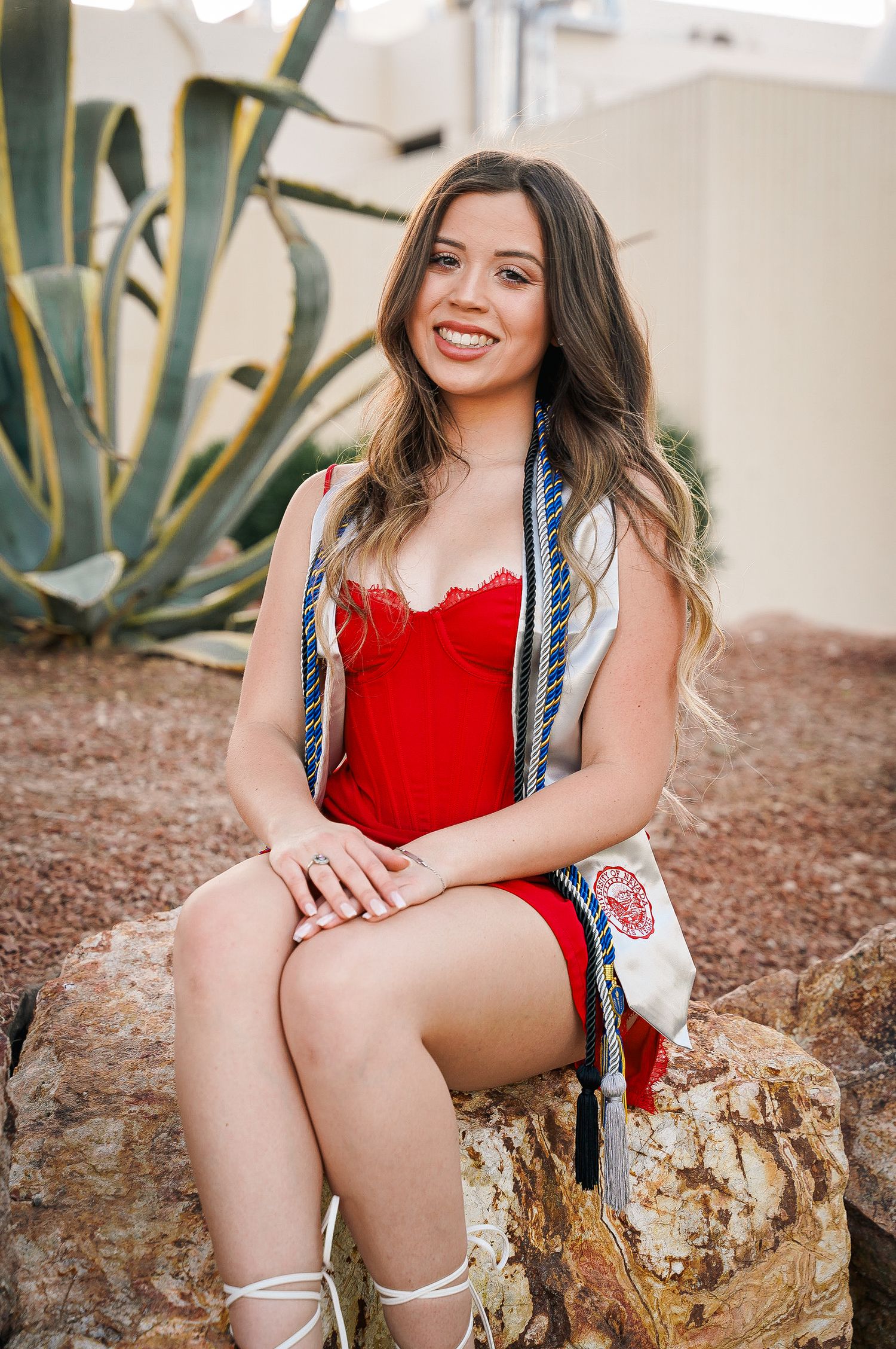 Outdoor graduation portrait with agave plant and stone wall background.