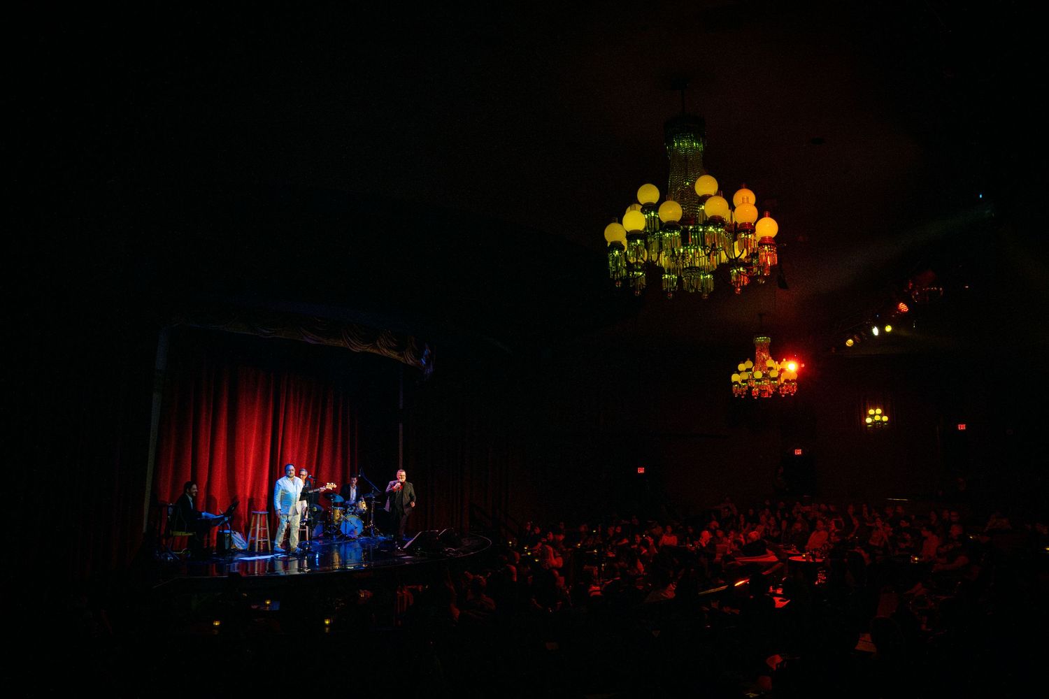 Dark theater stage illuminated by ornate chandeliers during performance.