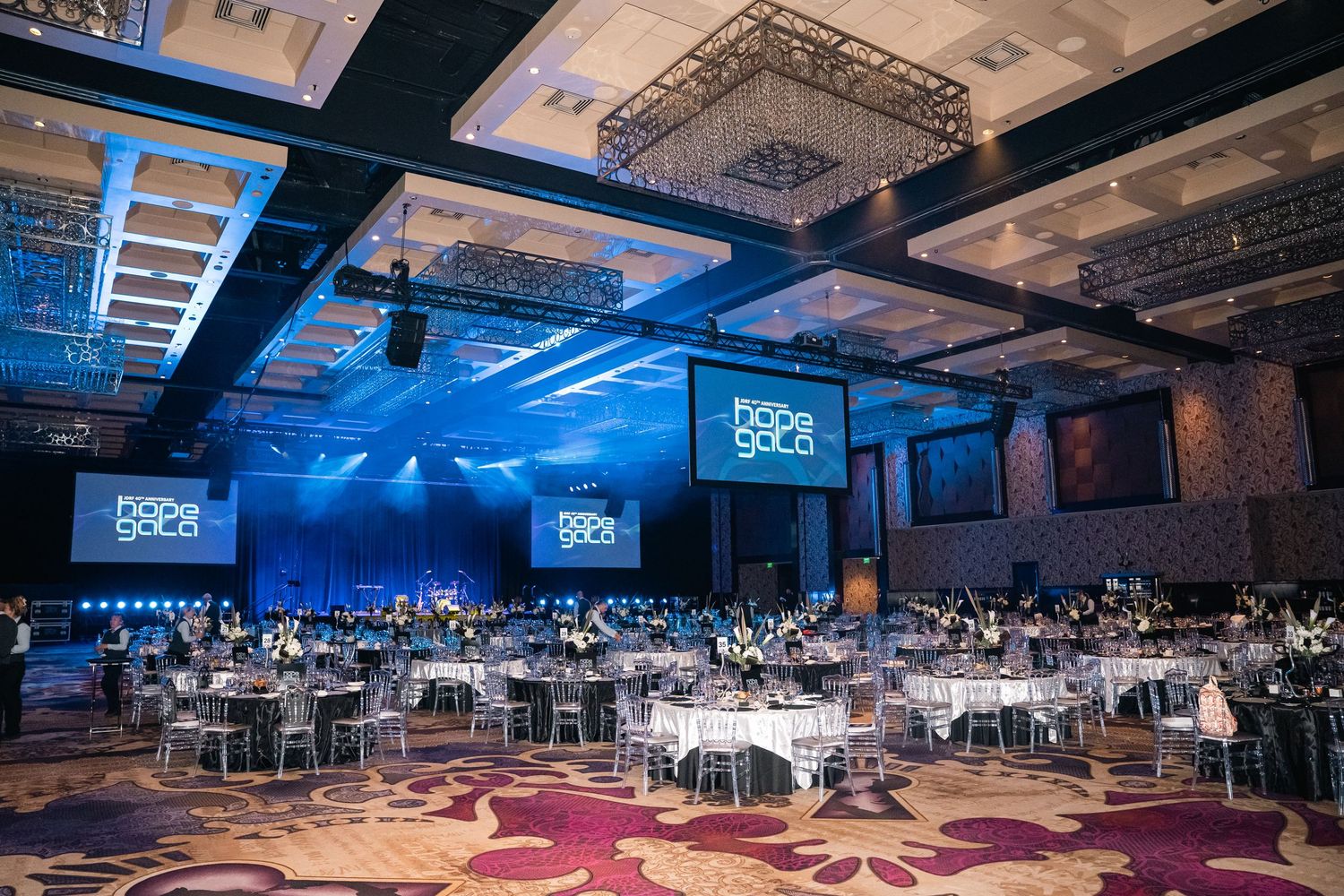 Grand ballroom set up for a gala dinner with blue lighting and multiple round tables.