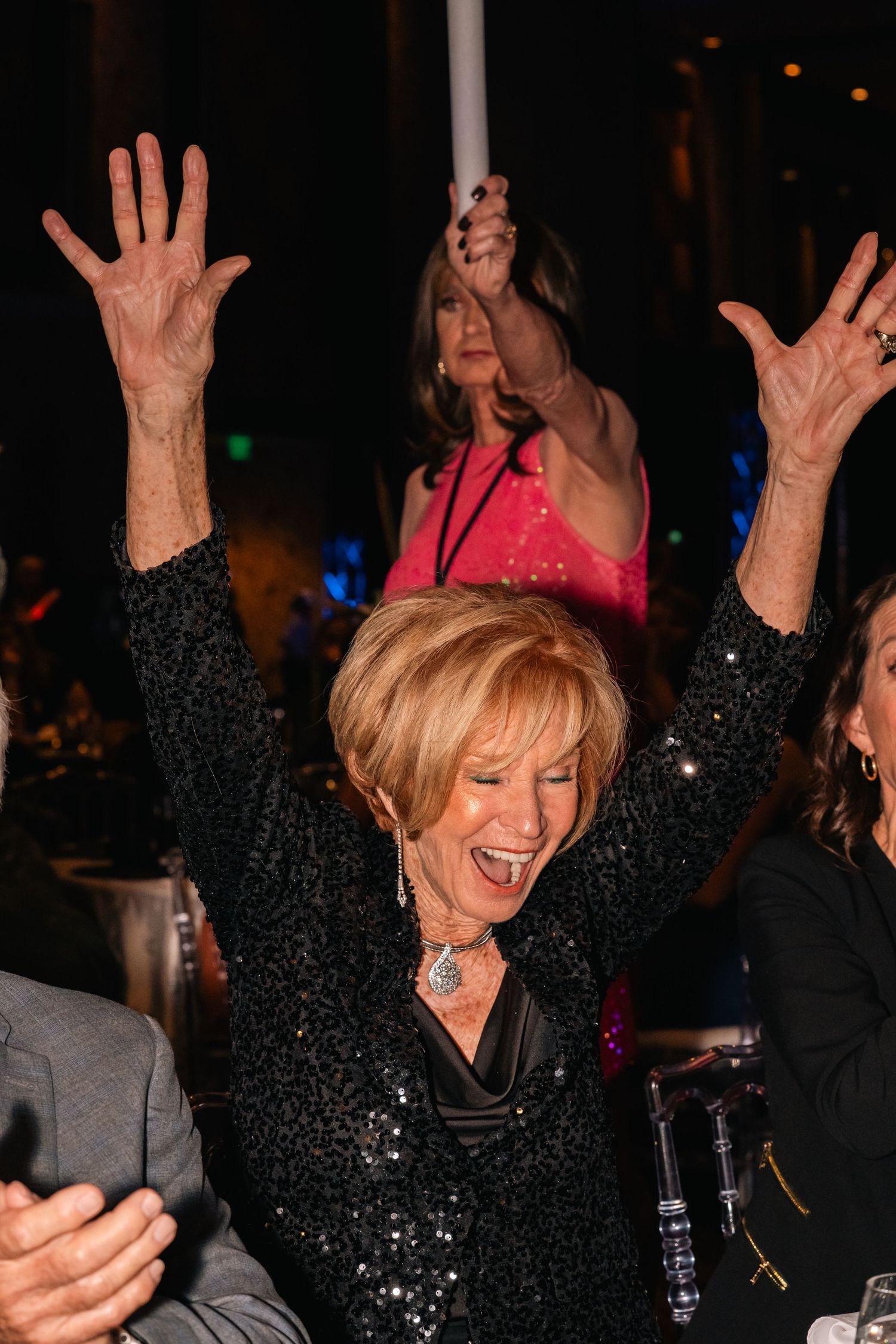 Attendee celebrating with arms raised at formal gala dinner event.