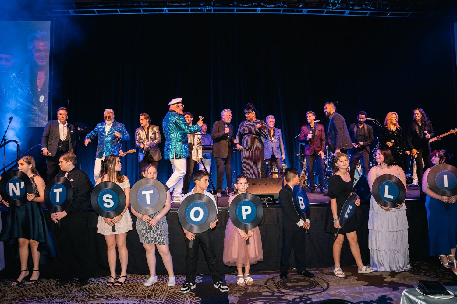 Group of performers standing together on stage with coordinated letter shirts spelling a message.