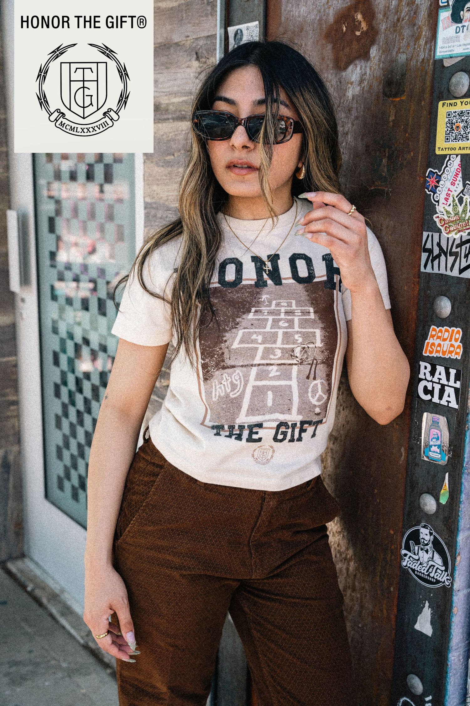 Urban streetwear fashion display featuring brown overalls and graphic t-shirt against brick wall.