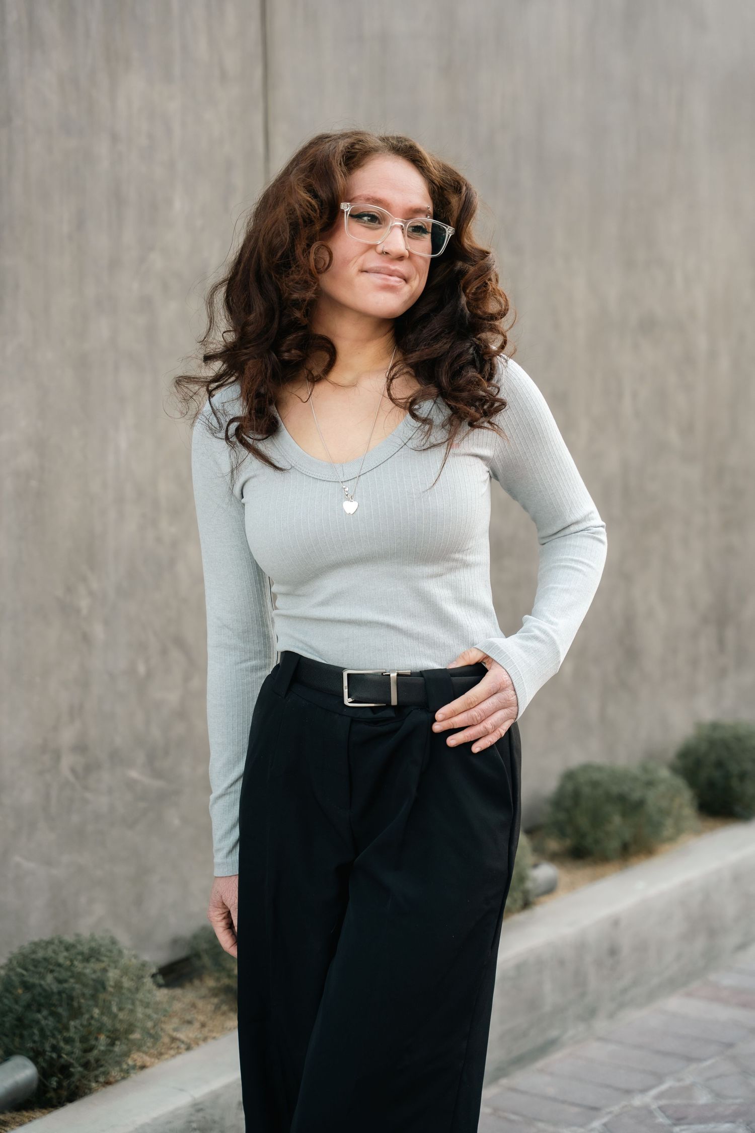Professional portrait of someone in a gray sweater and black pants with glasses.