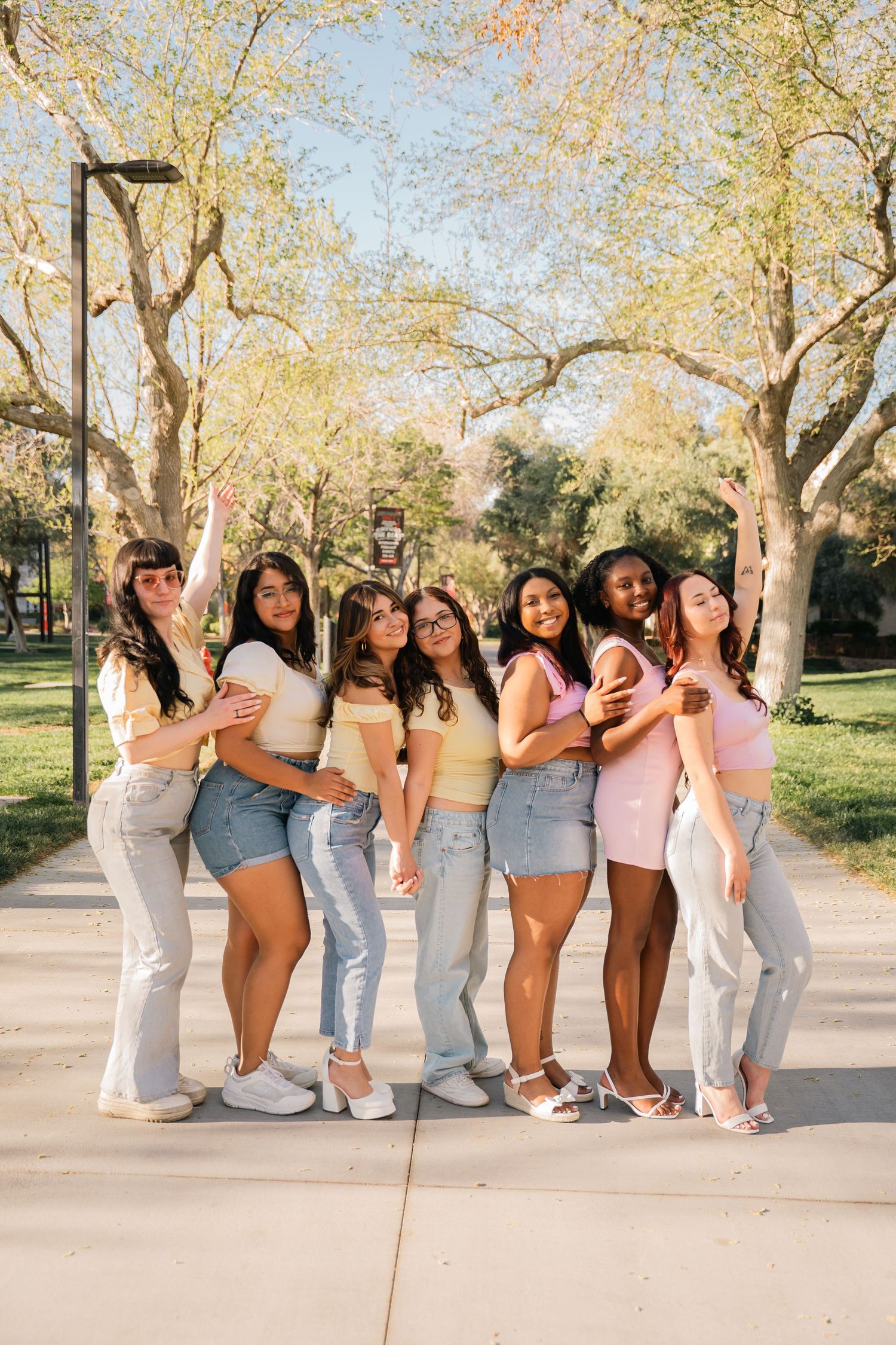Group of friends in casual outfits pose together on sunny park path.