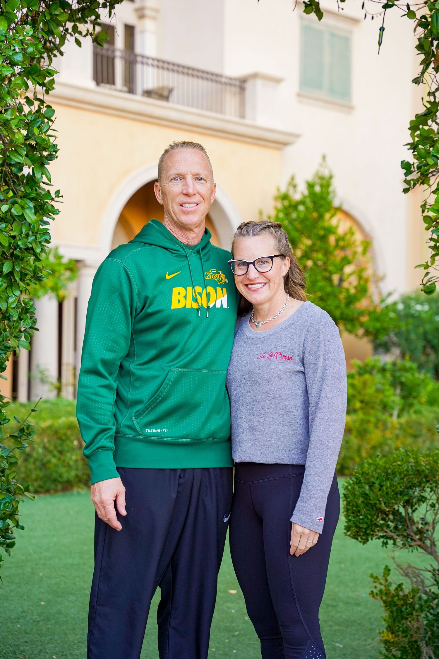 A pair wearing NDSU Bison and college apparel pose together on campus grounds.