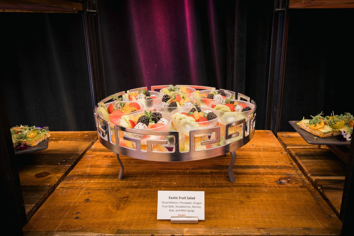Circular display of elegant appetizers arranged on tiered wooden platform with description card.
