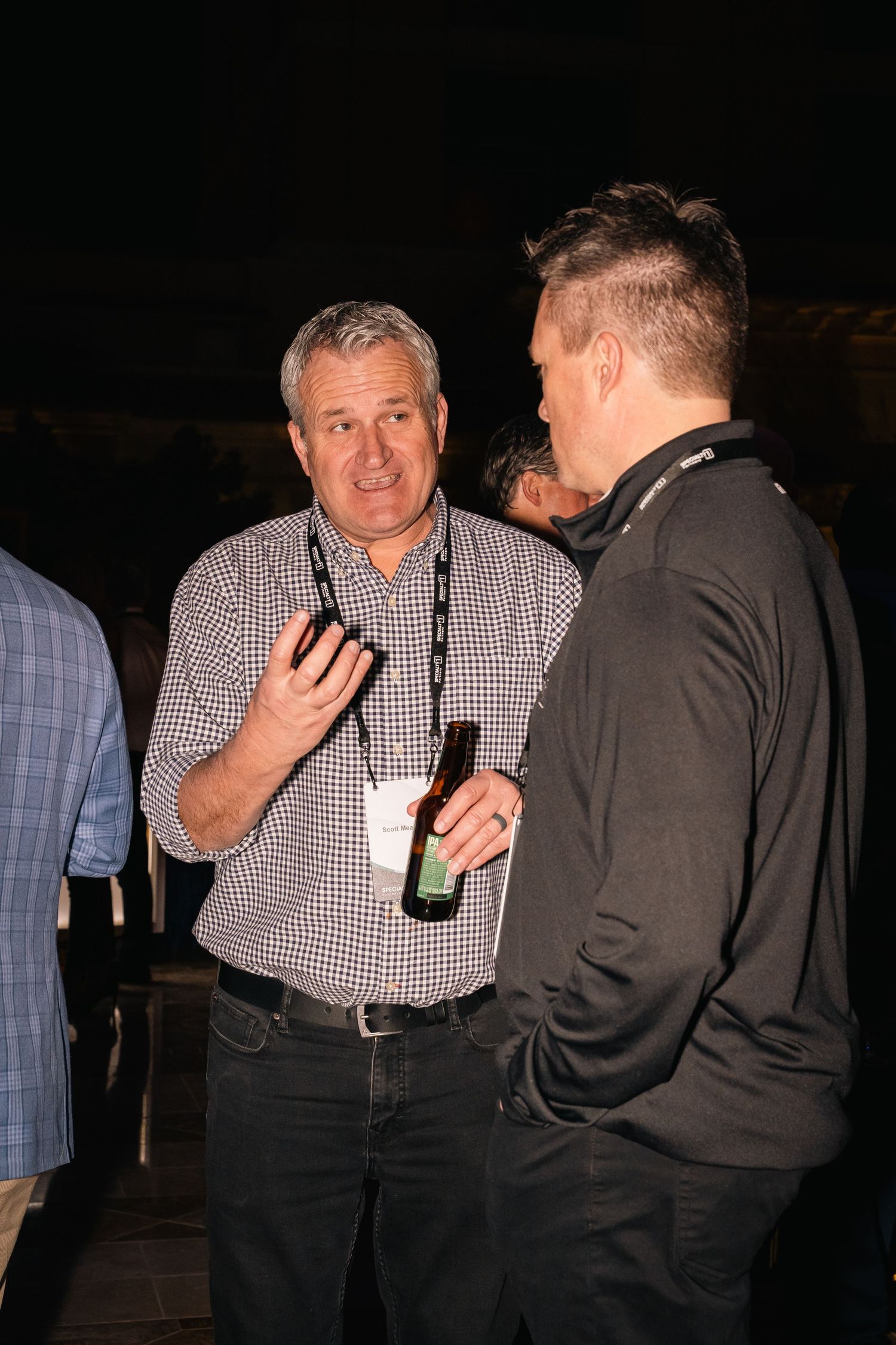 Two men engaged in conversation while holding drinks at evening social gathering.