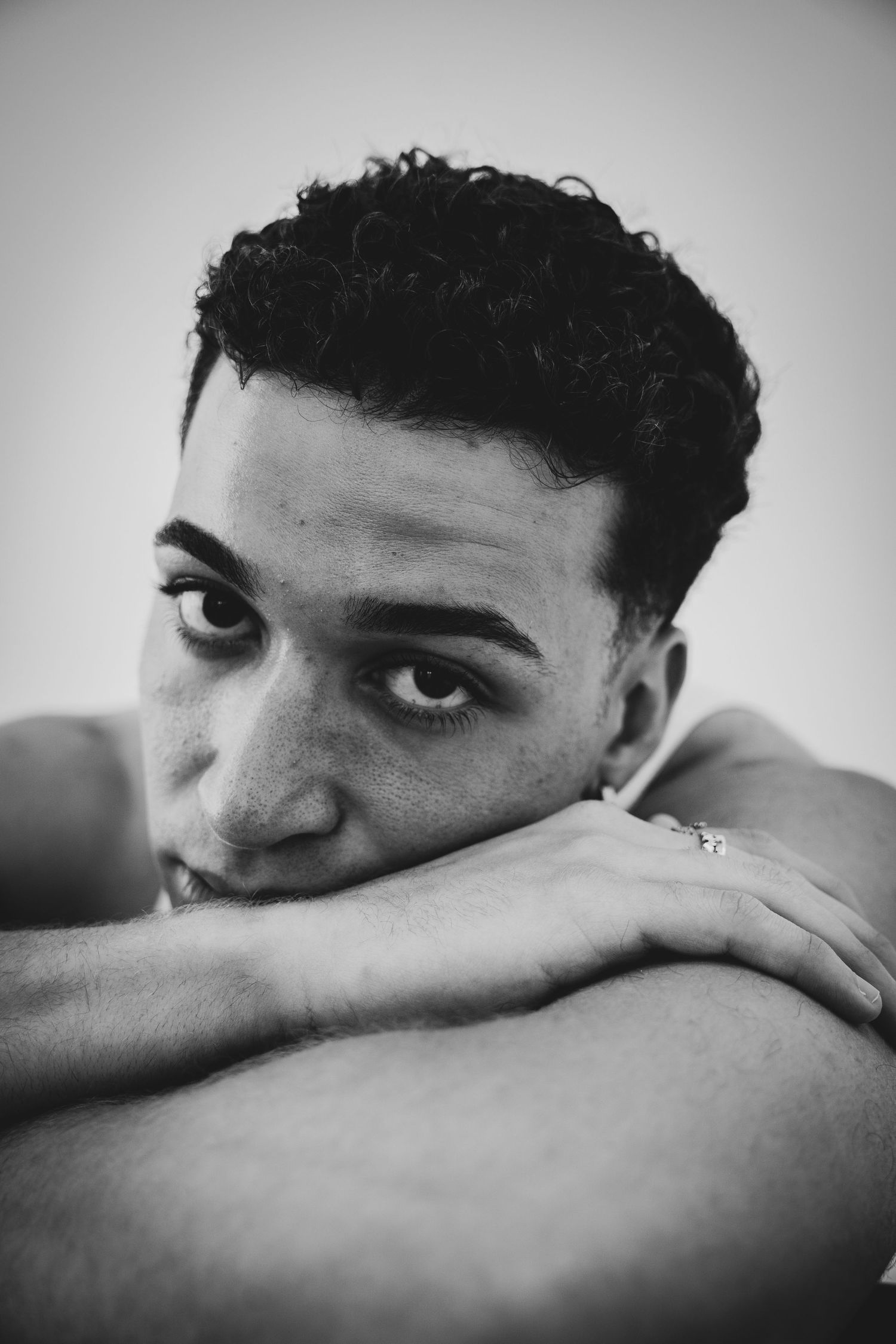 Black and white portrait of a model resting their head on crossed arms with a contemplative expression.