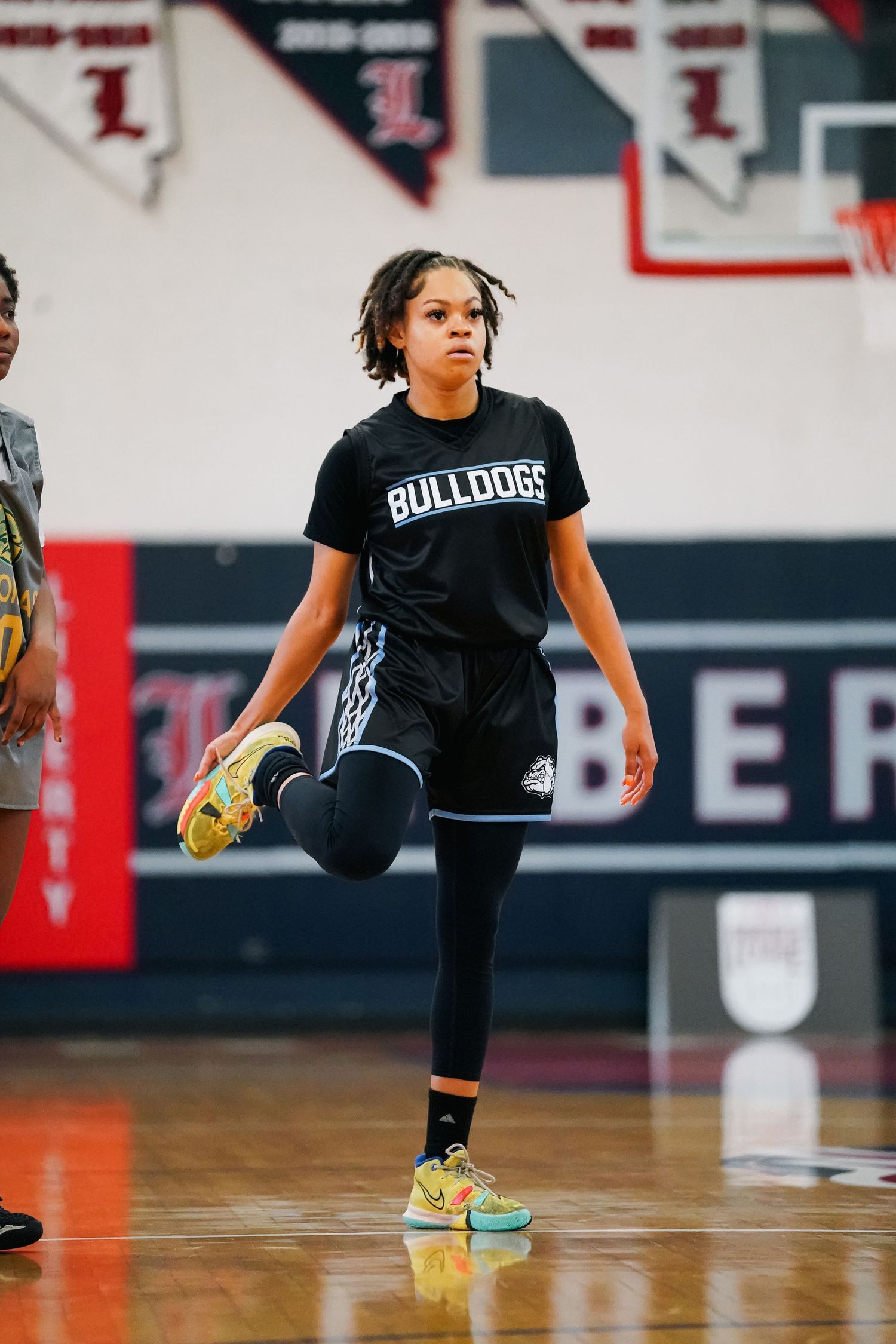 Athlete in black Bulldogs uniform performs defensive stance during basketball practice.