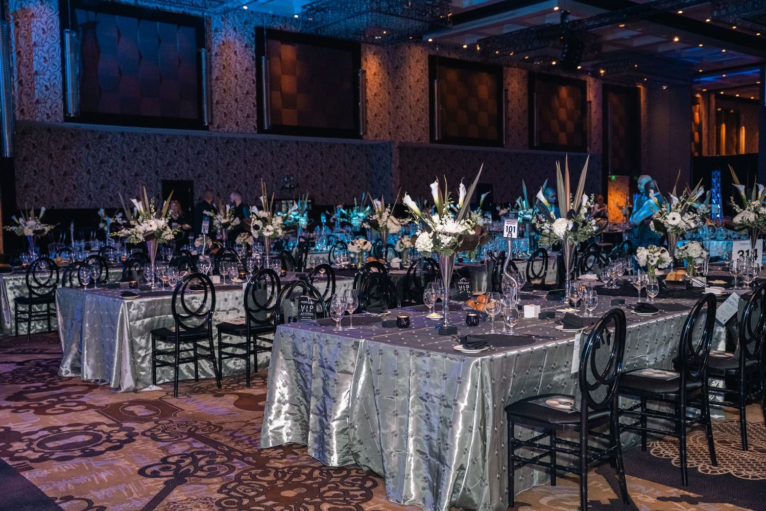 Elegant ballroom setup with silver tablecloths and black chairs for a formal dinner event.