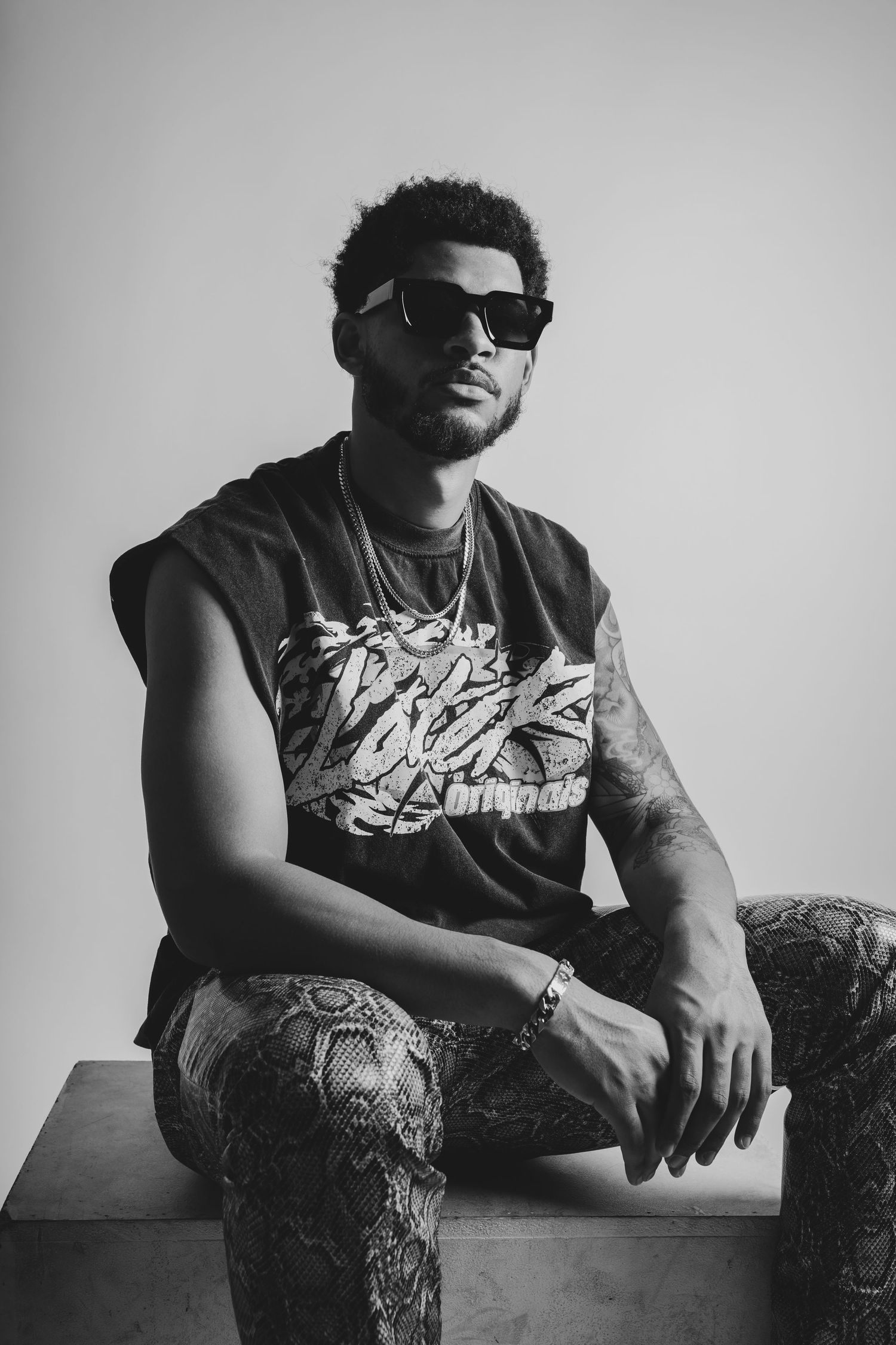 Monaco Media. Artistic black and white portrait of person in graphic tee and sunglasses sitting on platform.