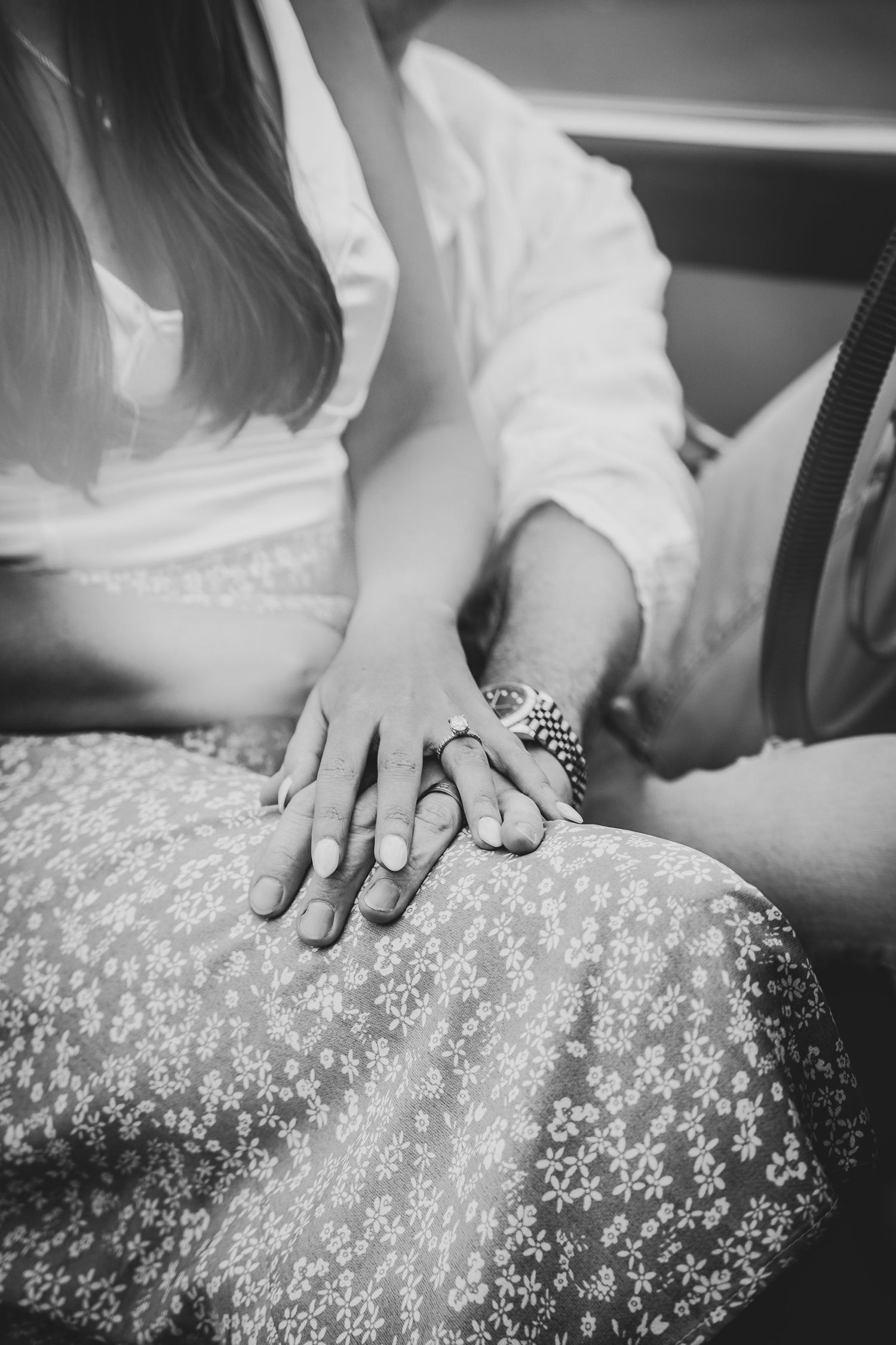 Black and white photo of hands with engagement ring resting on floral patterned dress.