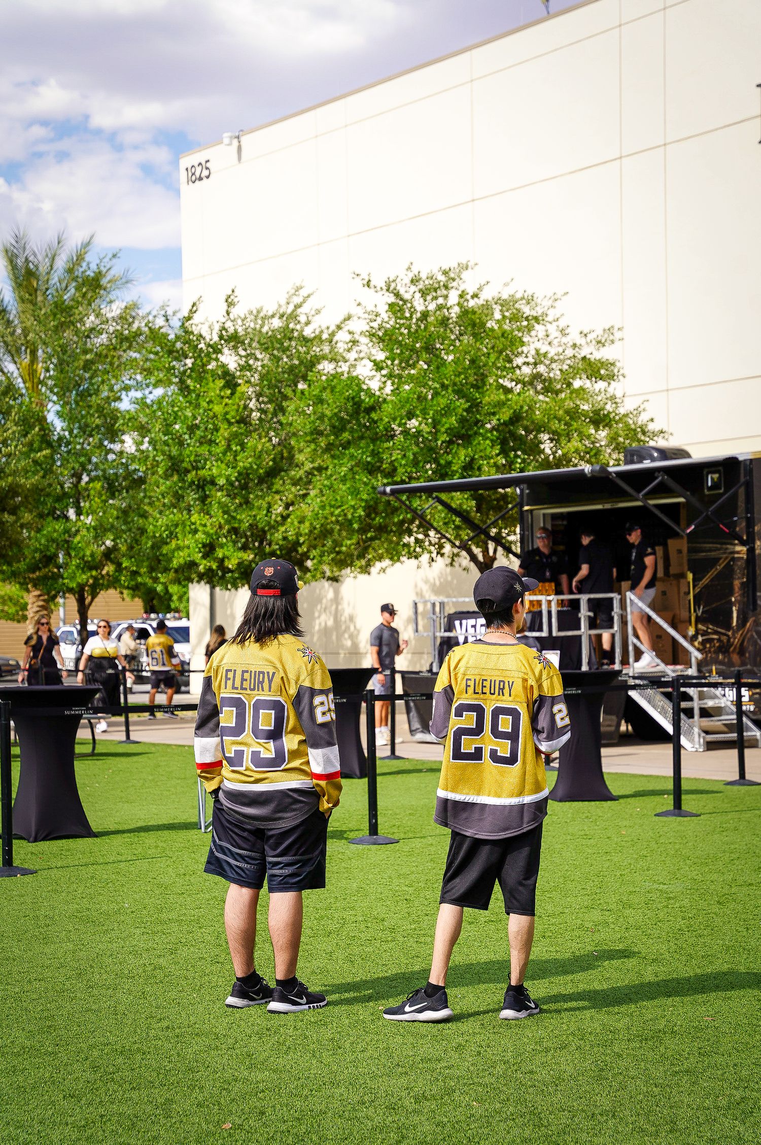 Two fans wearing matching yellow hockey jerseys stand on artificial turf at an outdoor event.