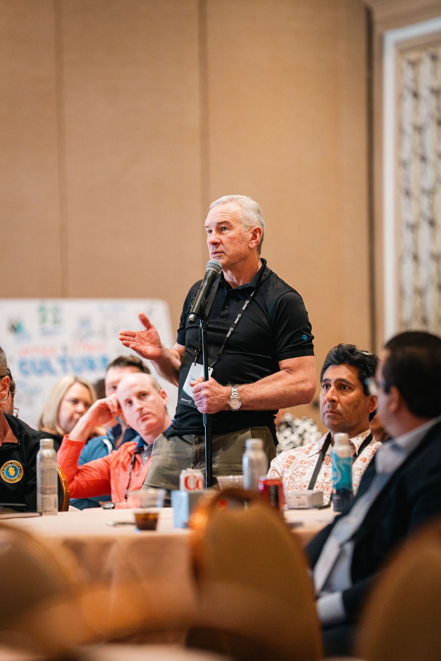 Professional speaker in black polo shirt gesturing while addressing audience at business conference event.