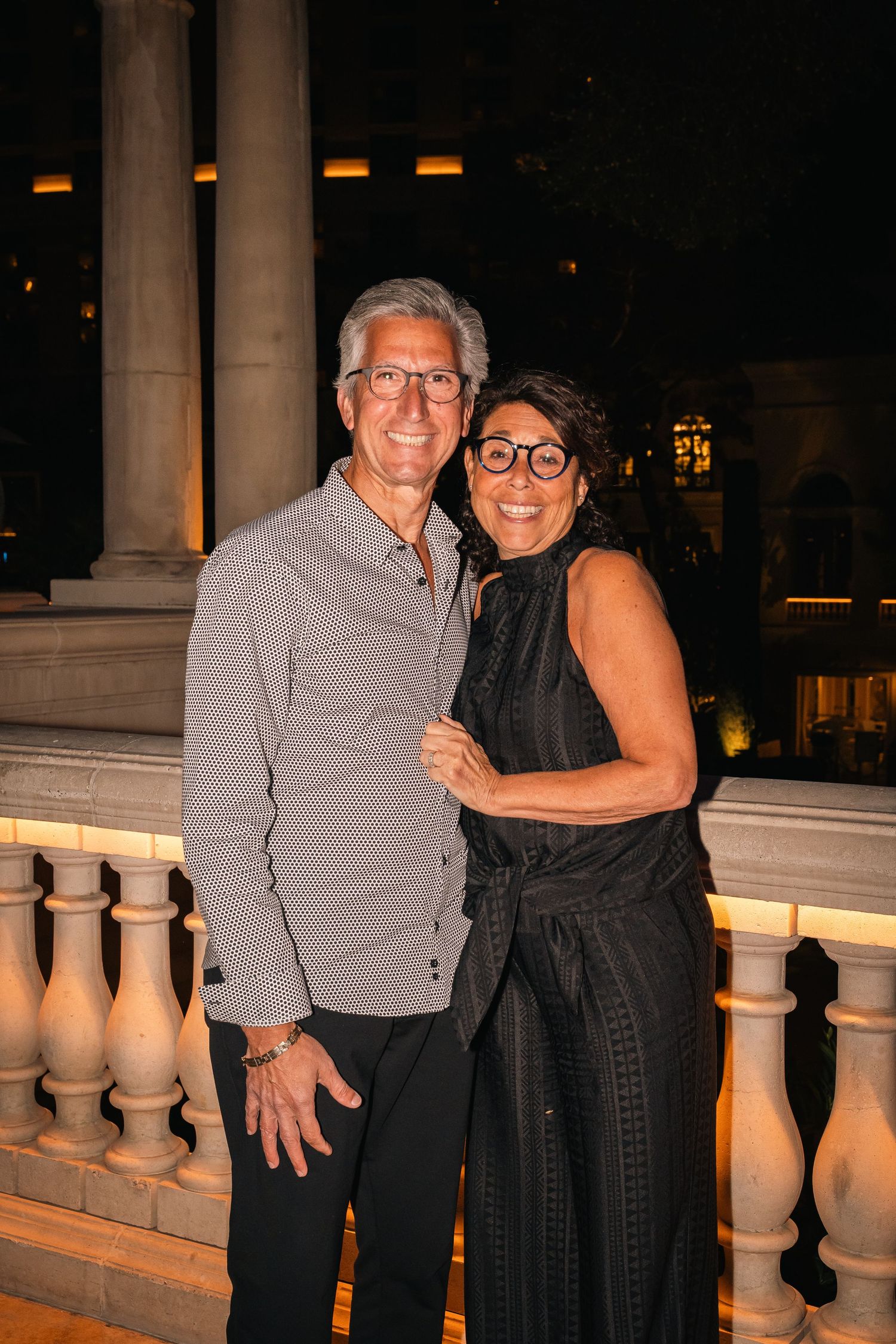 Couple poses together at an elegant evening event near ornate balustrade.