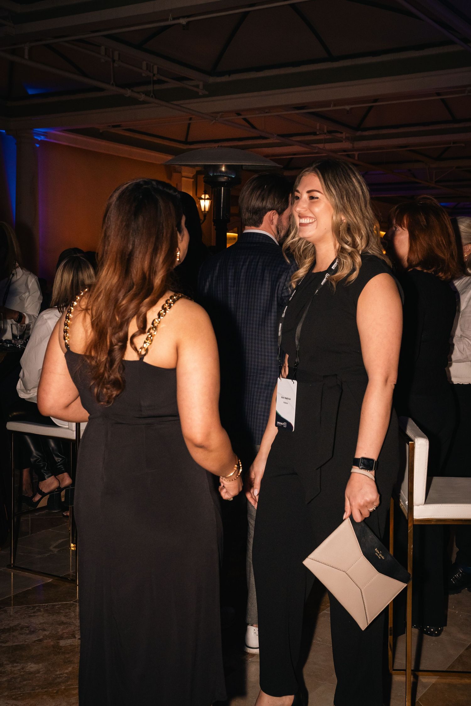 Two women in black dresses engage in conversation at an evening networking event.