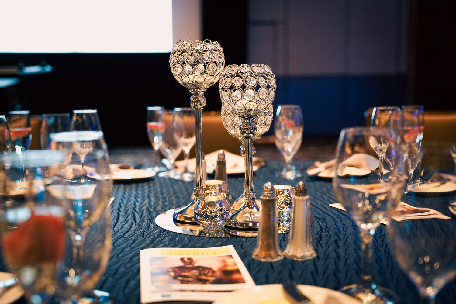 Elegant crystal stemware and place settings on blue tablecloth at formal dinner event.
