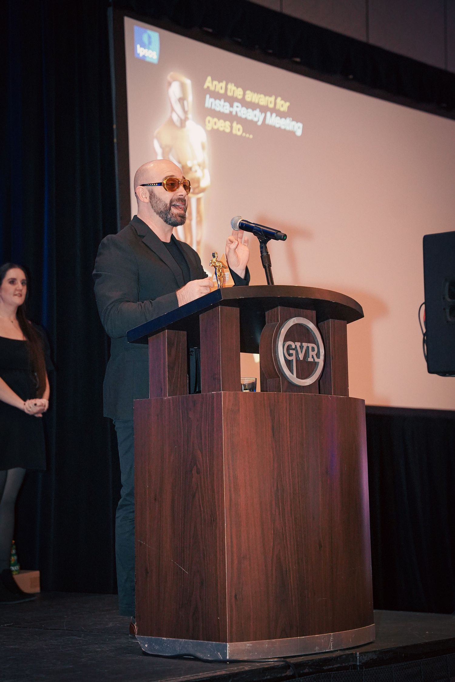 Speaker presenting at wooden podium during corporate event with projection screen.