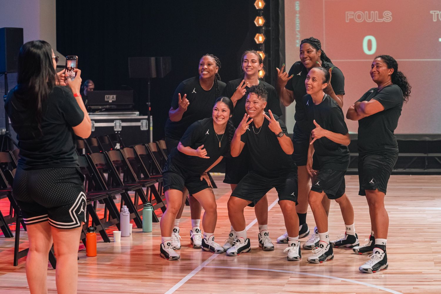 Basketball team celebrating together on sidelines of indoor court during practice.