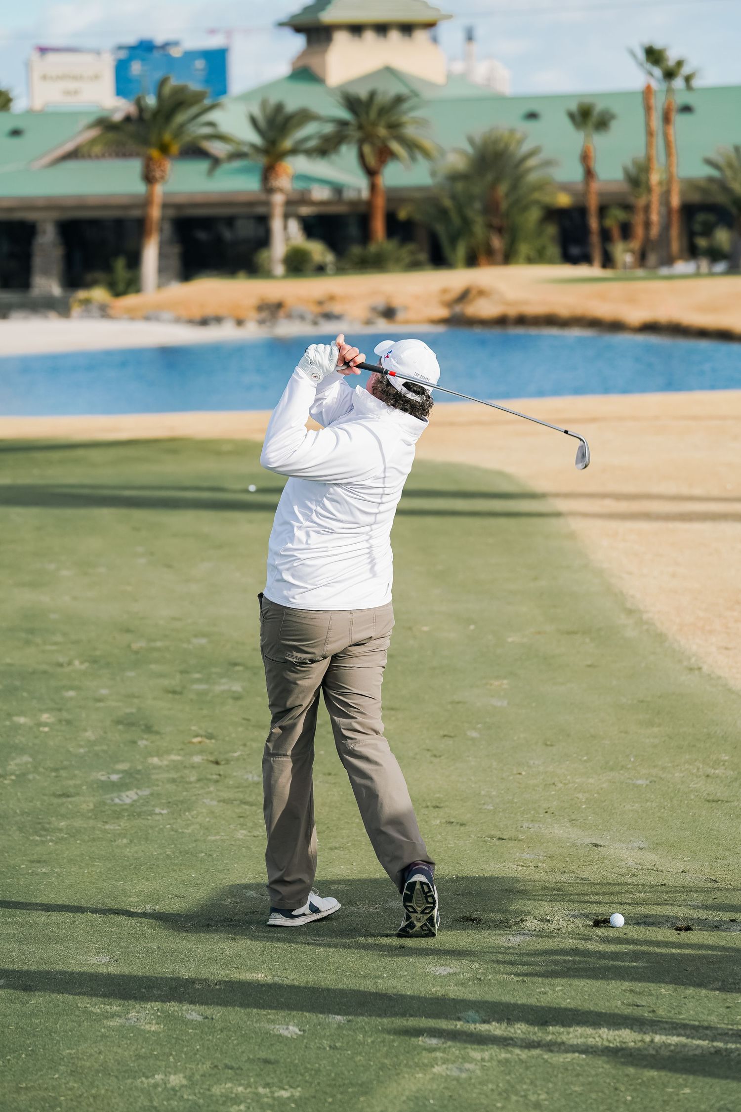 Golfer taking a swing on a golf course with a lake and resort buildings in the background.