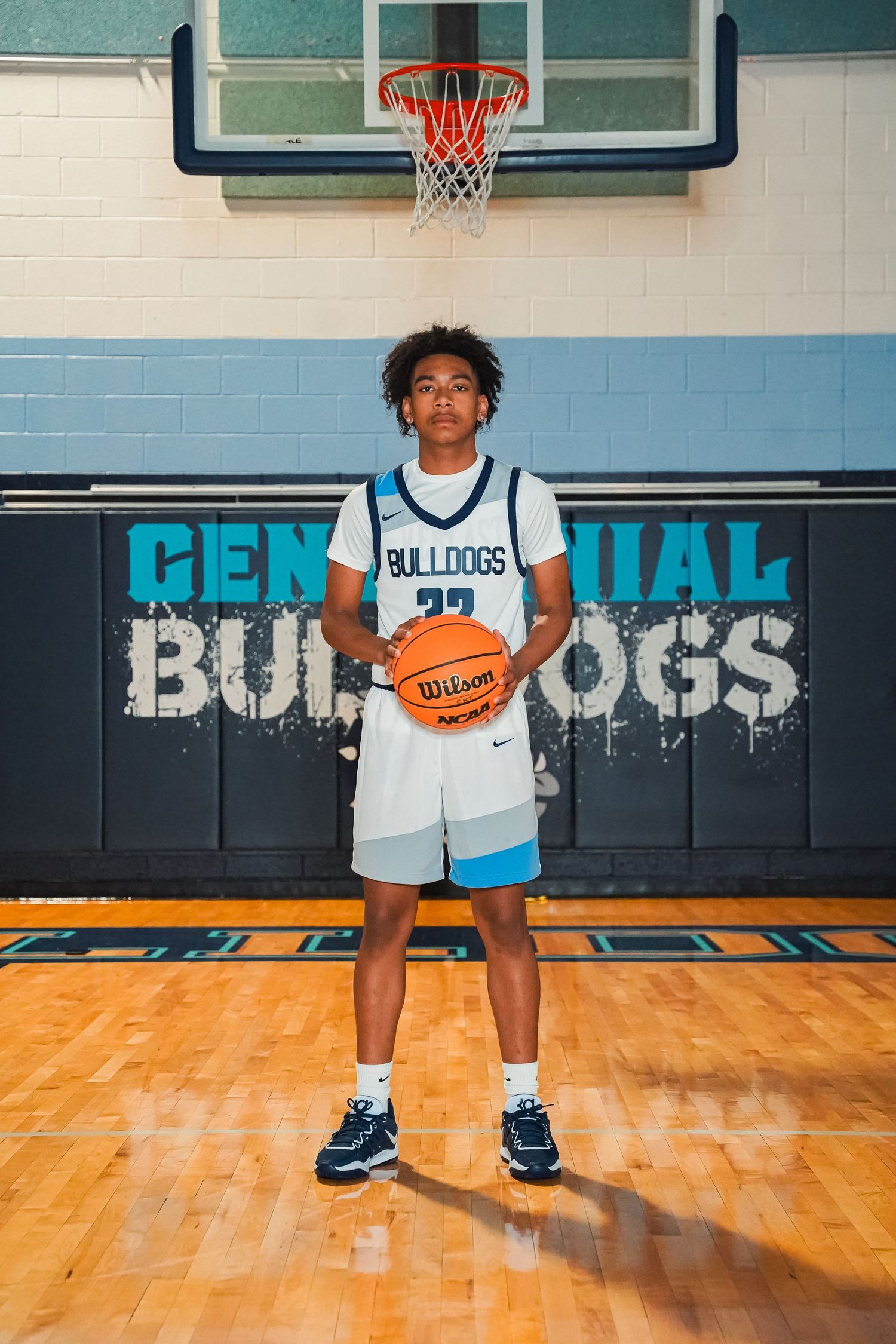 Basketball player holds ball while standing in front of Centennial Bulldogs wall signage.