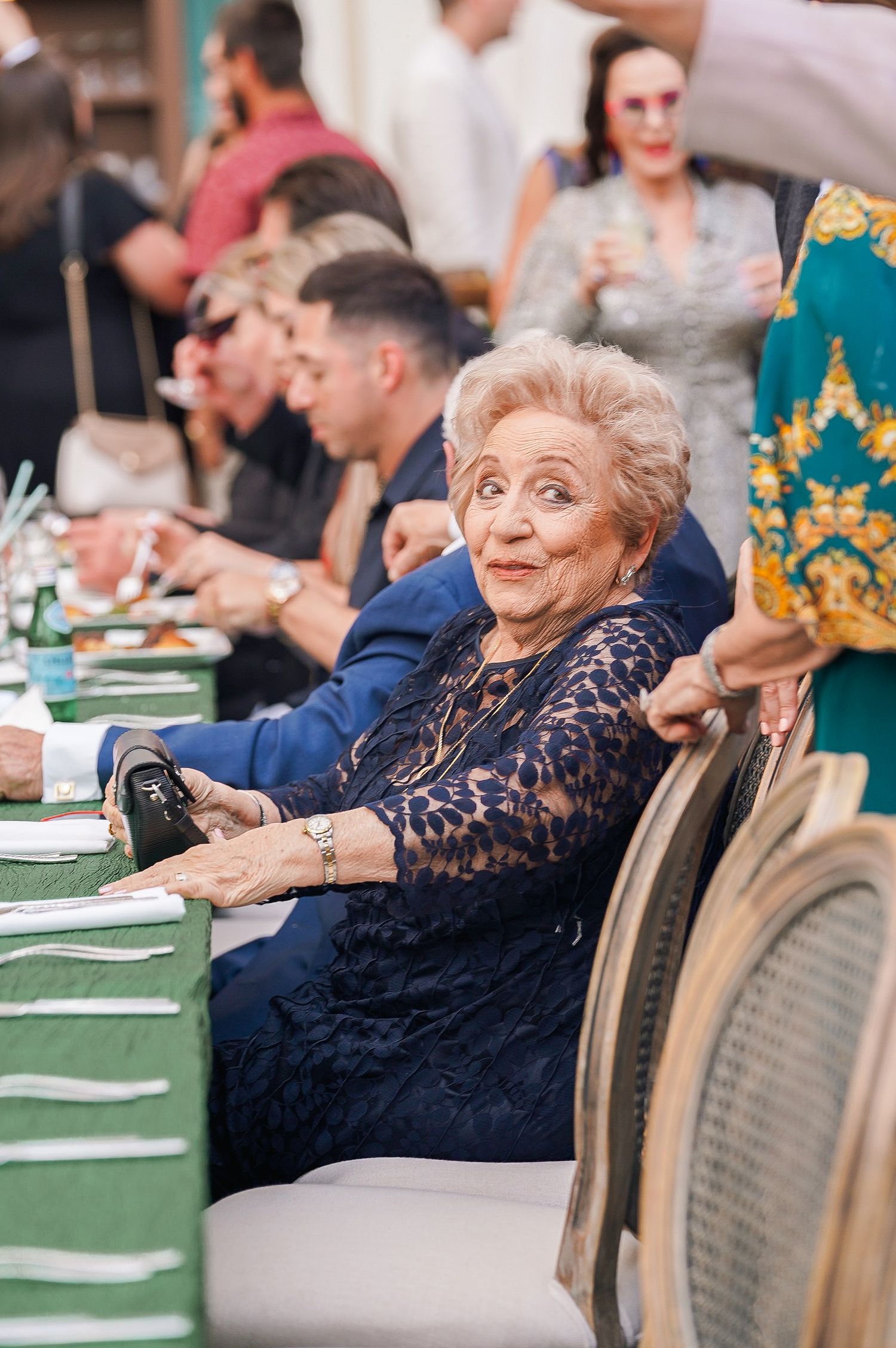 Elderly guests in formal attire seated at elegant dining tables with green tablecloths.