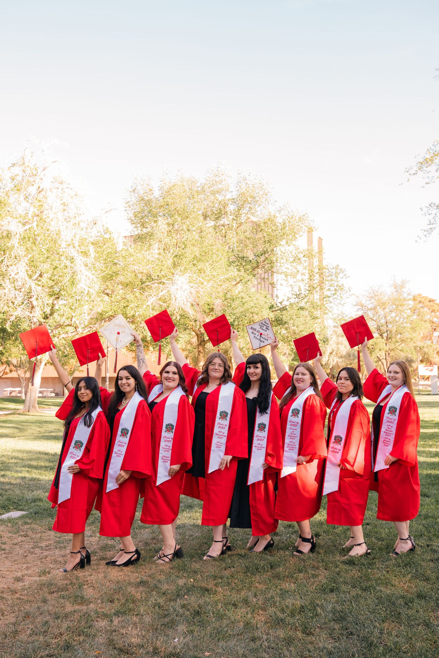 Graduates in red caps and gowns toss their caps joyfully on a sunny lawn.