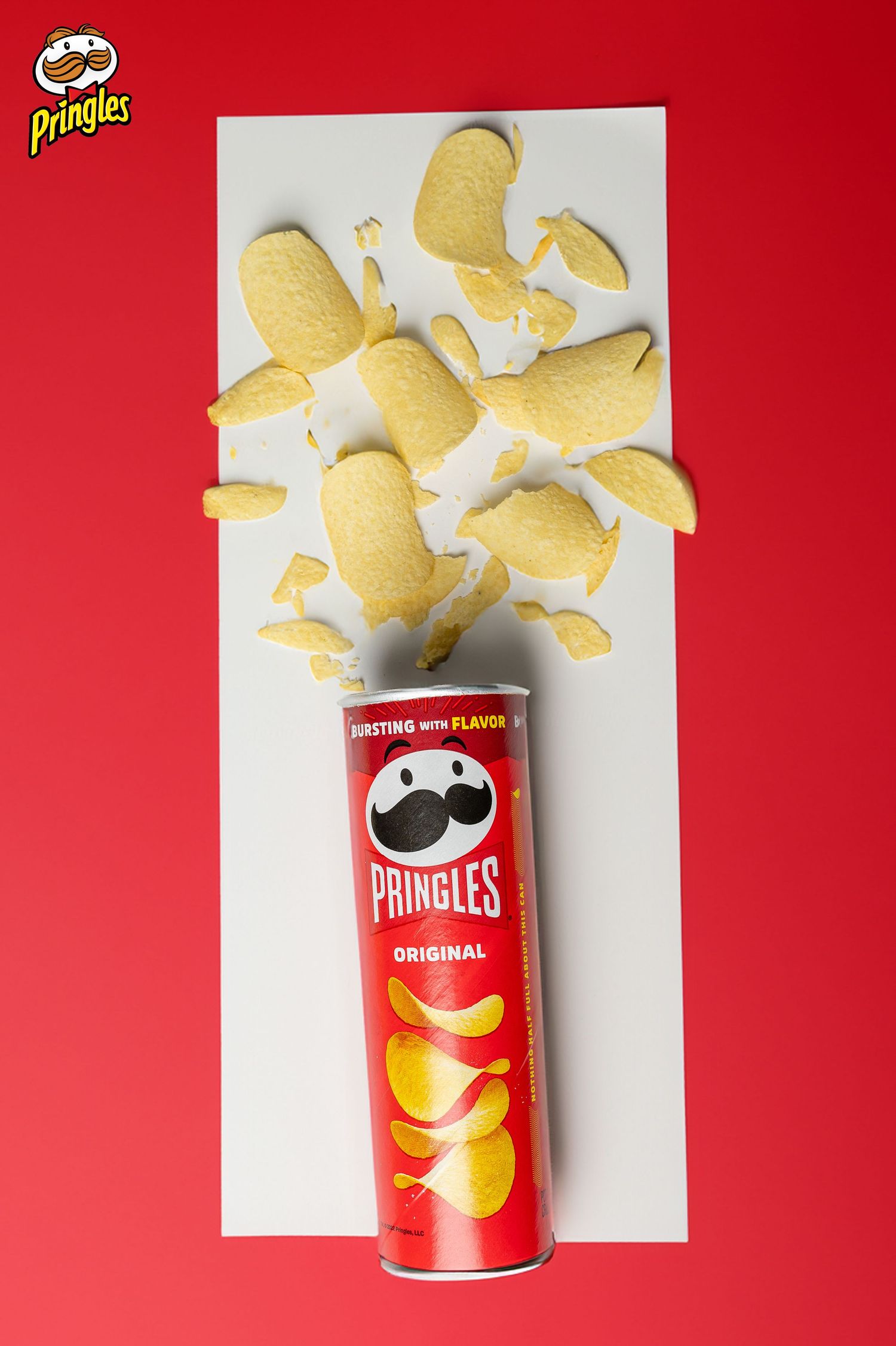Pringles original can with exploding chips against red background.