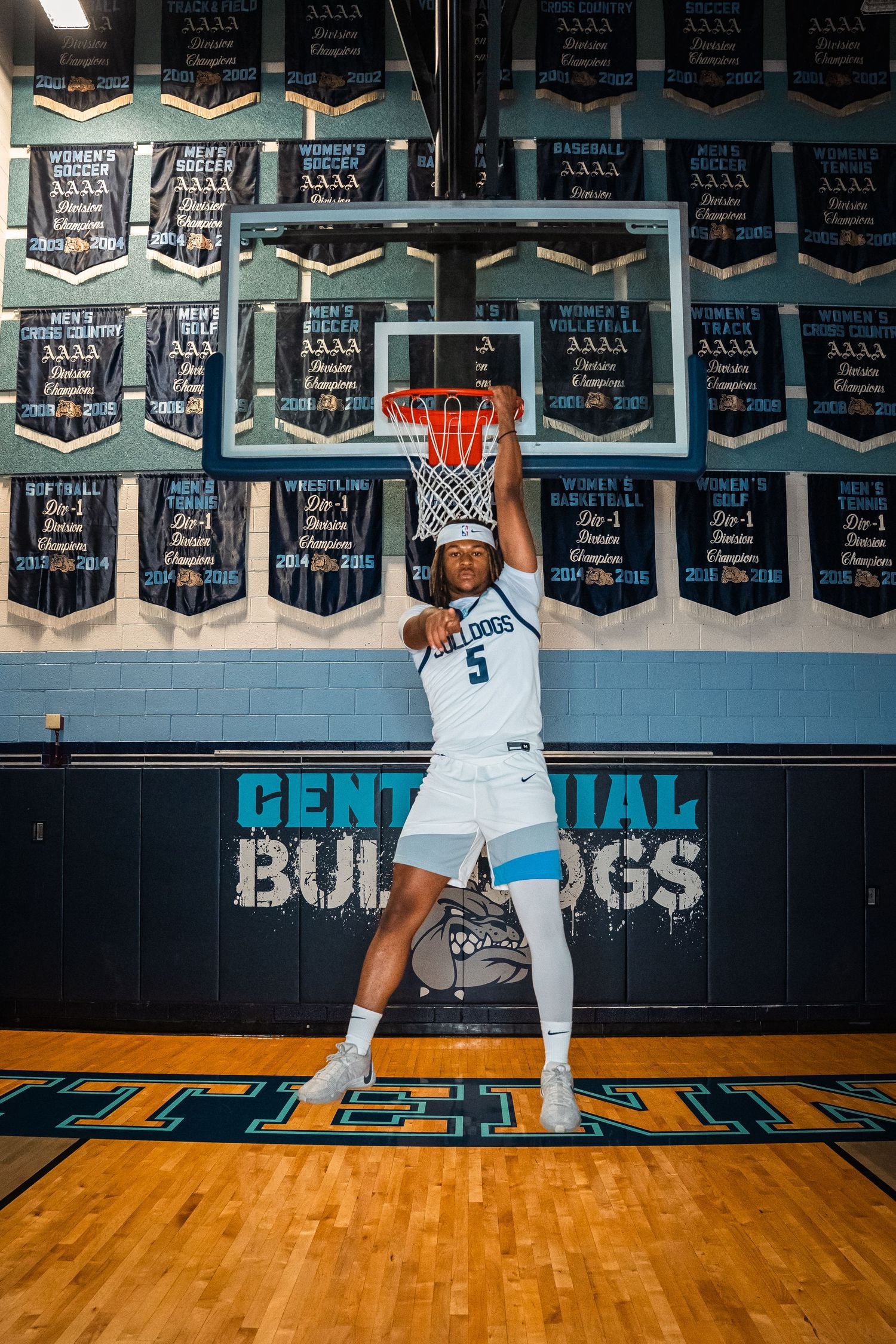 Basketball player in white uniform dunking basketball beneath championship banners.
