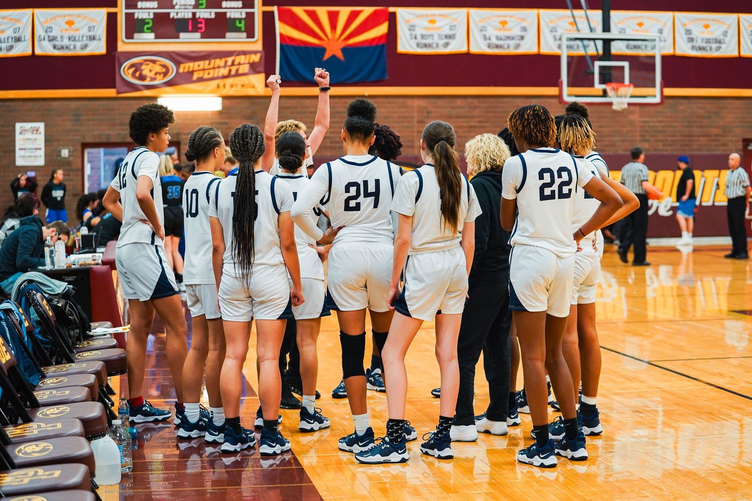 Basketball teams line up along the sideline in a gymnasium with Arizona state flag visible.