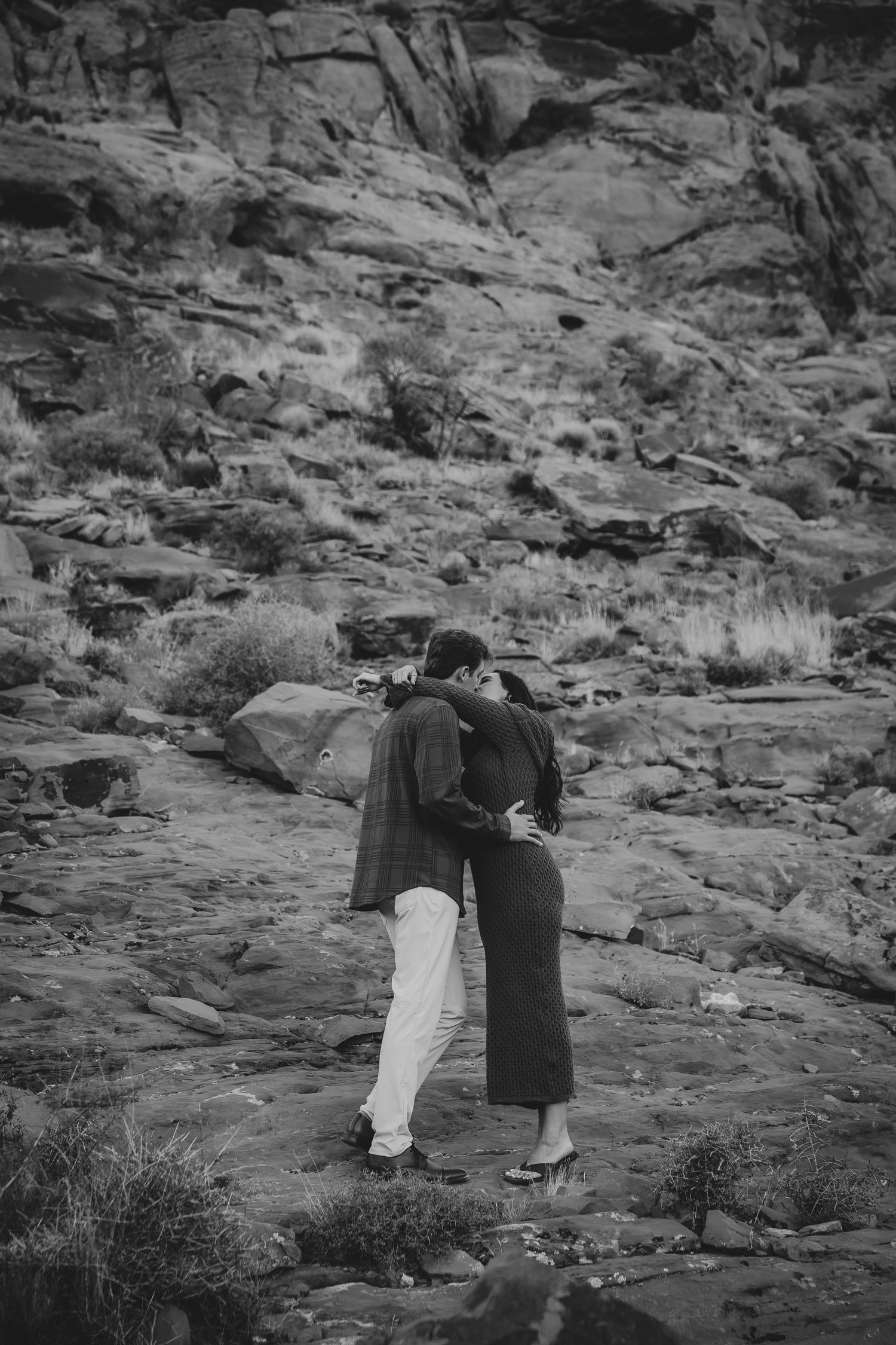 A black and white shot of a couple walking together along a dramatic desert cliff face.