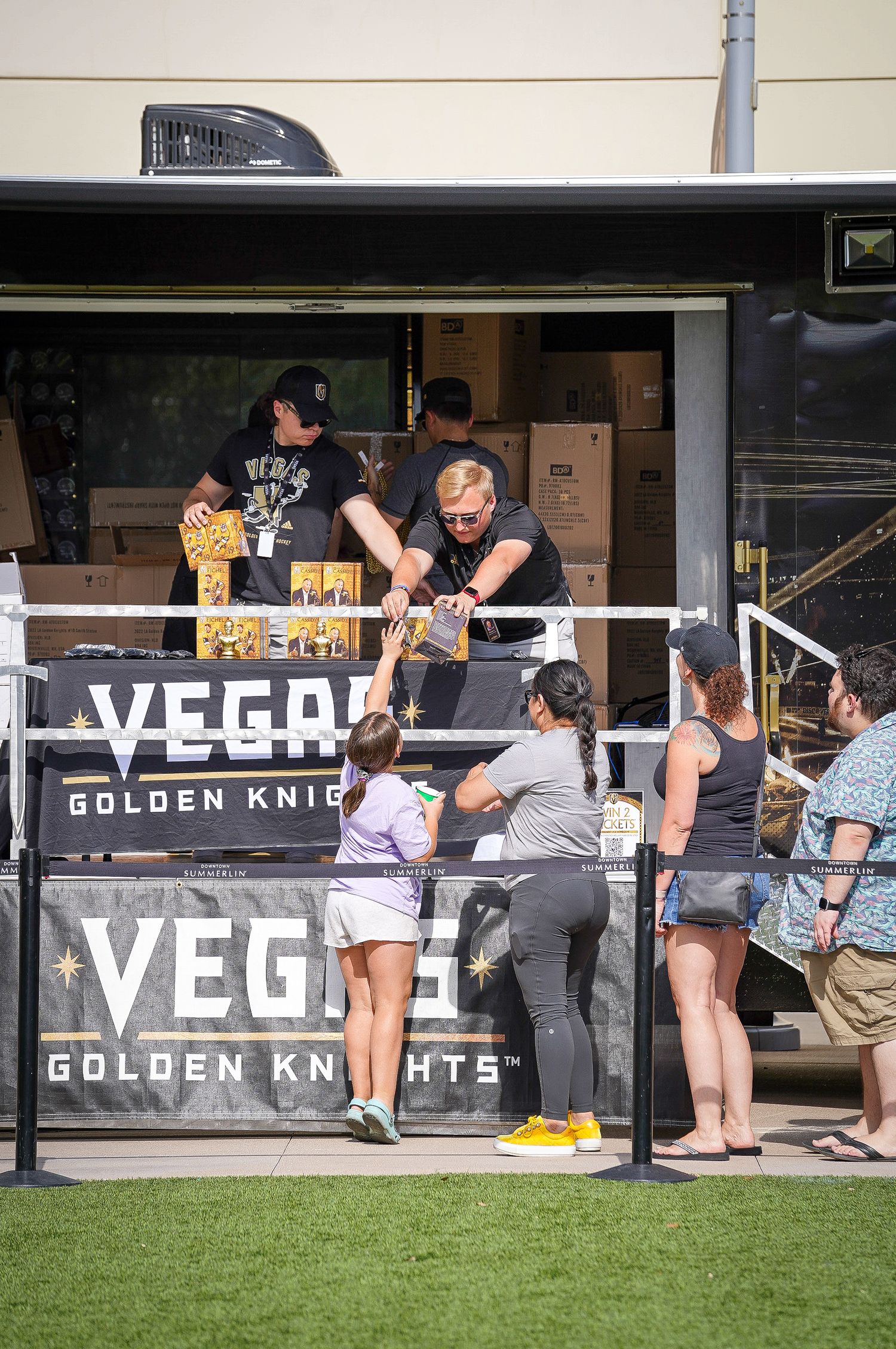 Staff serve customers at Vegas Golden Knights merchandise booth during outdoor event.