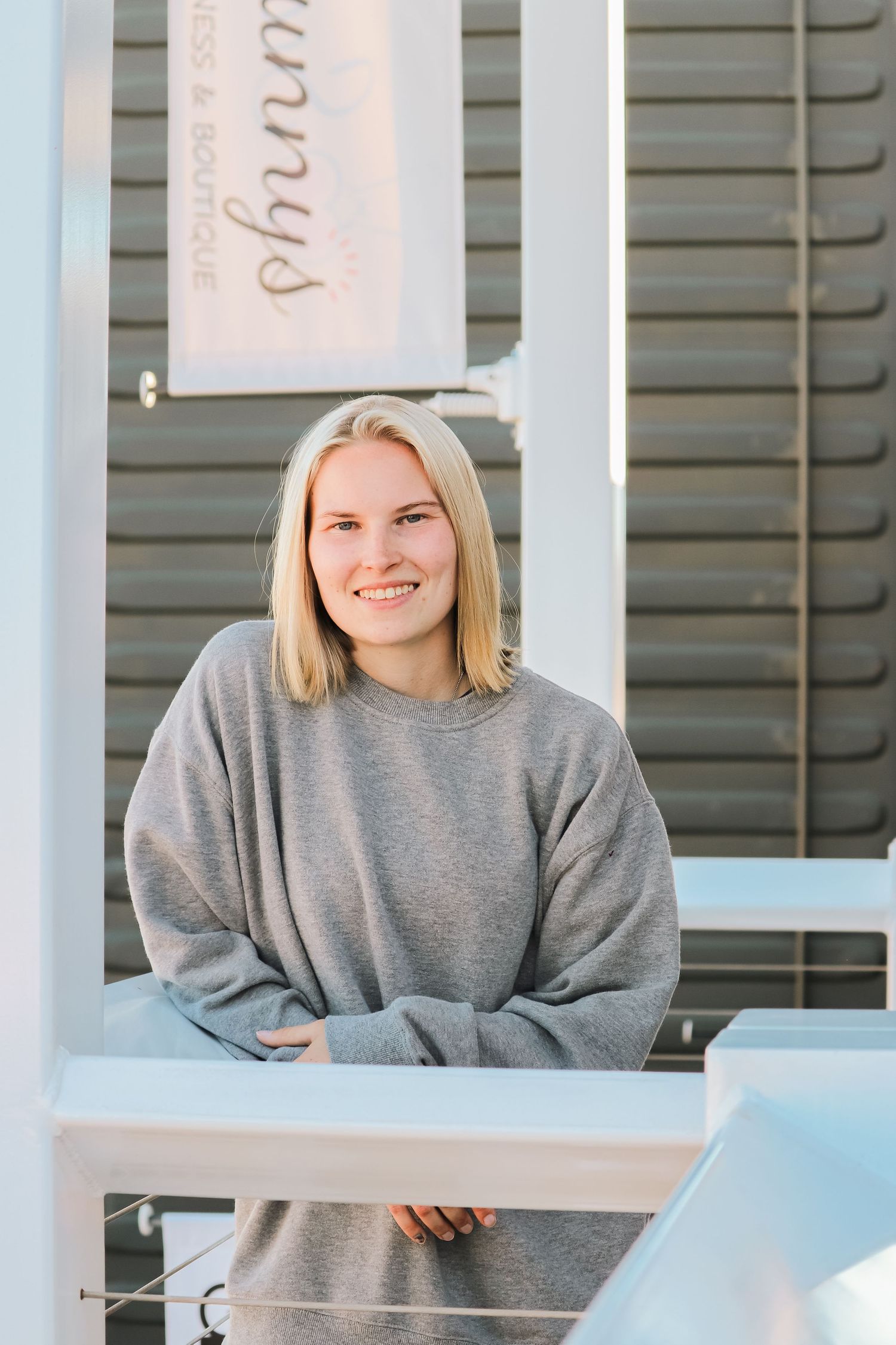 Person in casual gray sweatshirt smiling near architectural elements with white columns.
