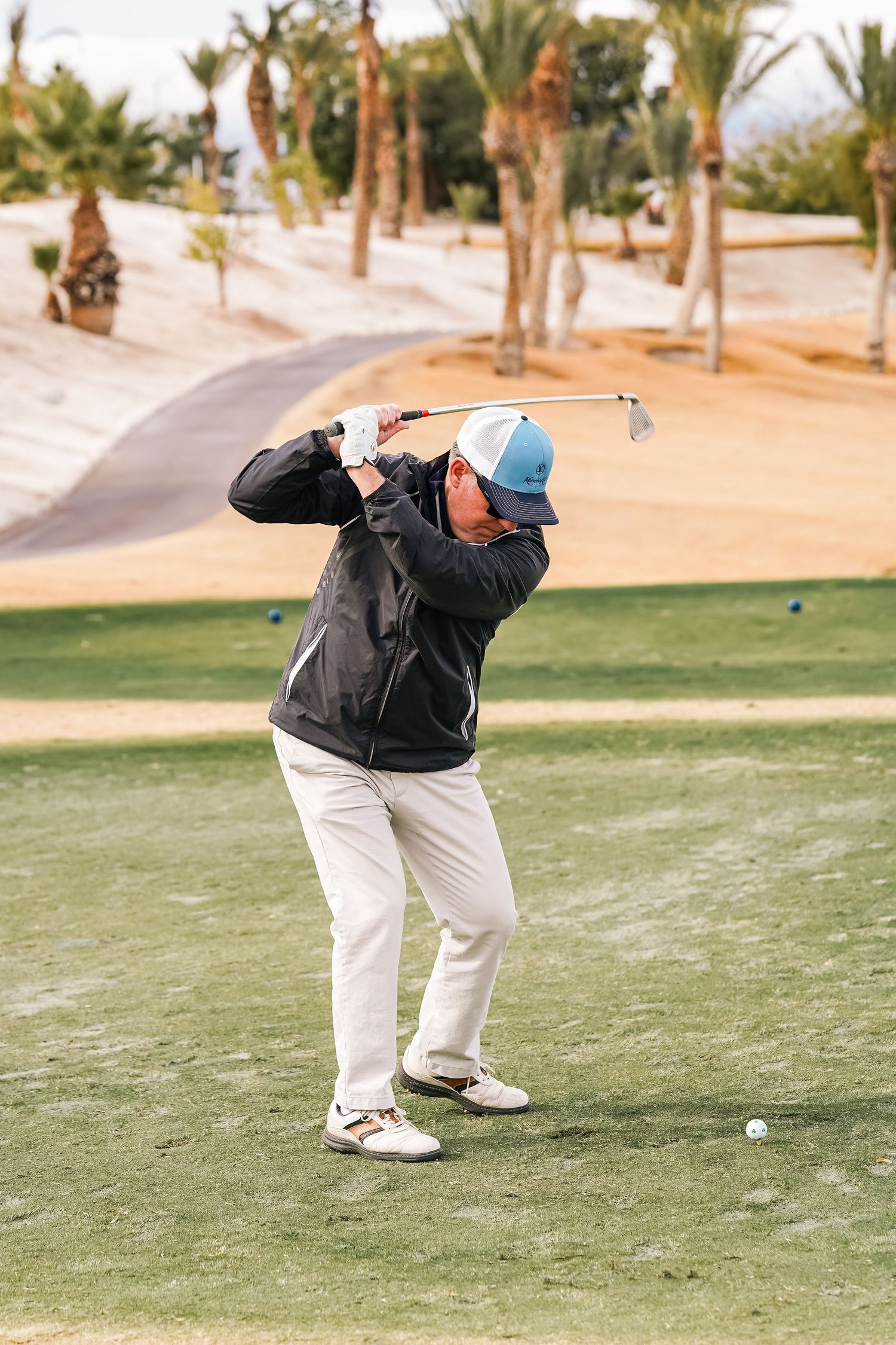 Golfer in black jacket and white pants demonstrates proper golf swing form.