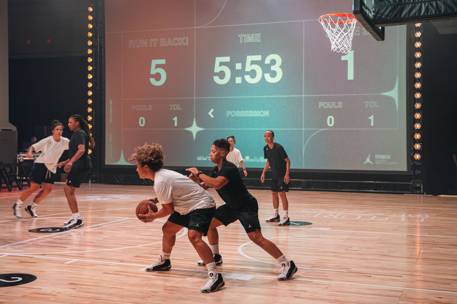Basketball players practicing on indoor court with scoreboard showing 5:53 remaining.