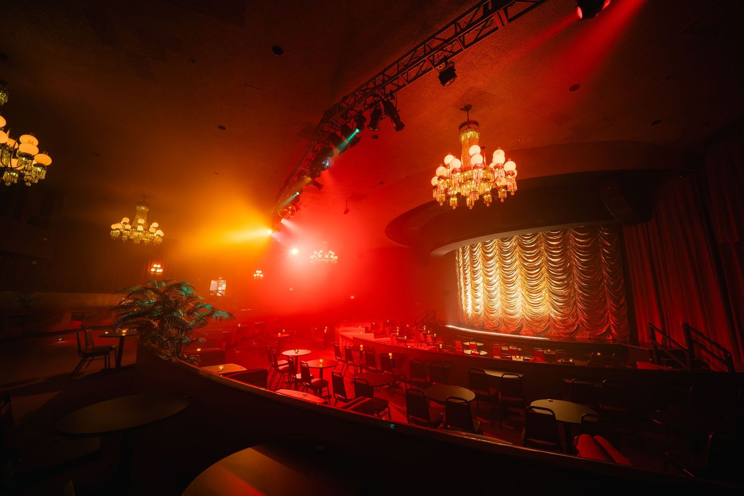 Vintage theater interior with ornate chandeliers bathed in warm red stage lighting.