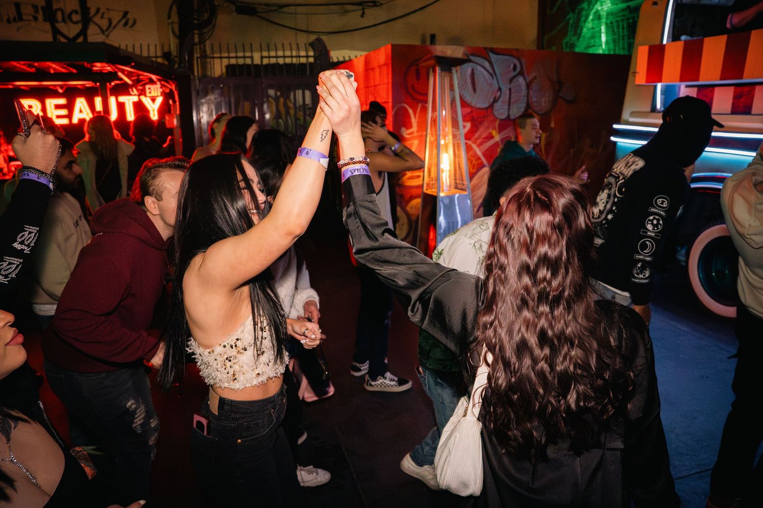 Crowd of people dancing and raising hands at a nightclub with neon lighting.