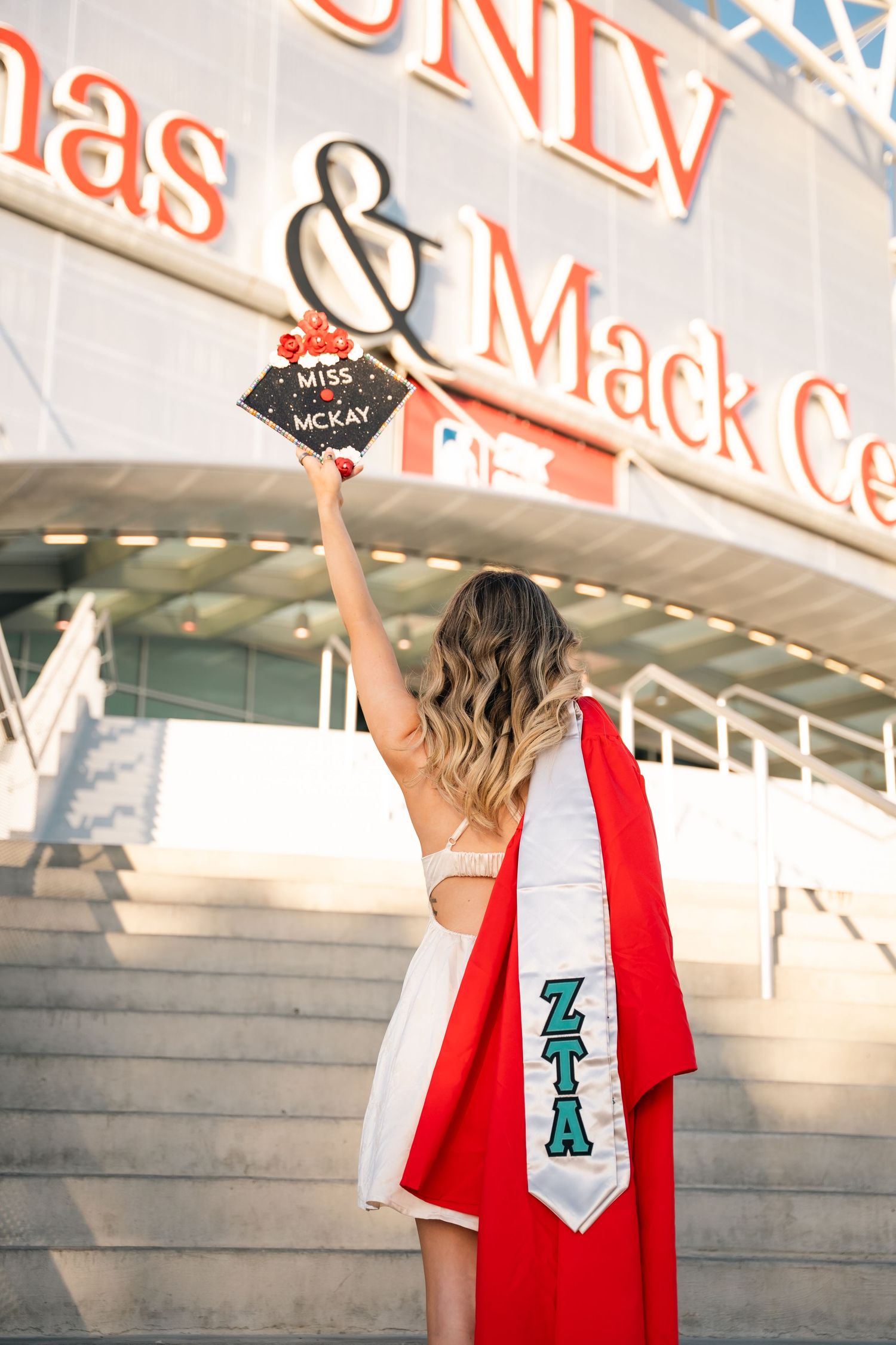 Graduate holding decorated graduation cap outside UNLV Thomas & Mack Center.