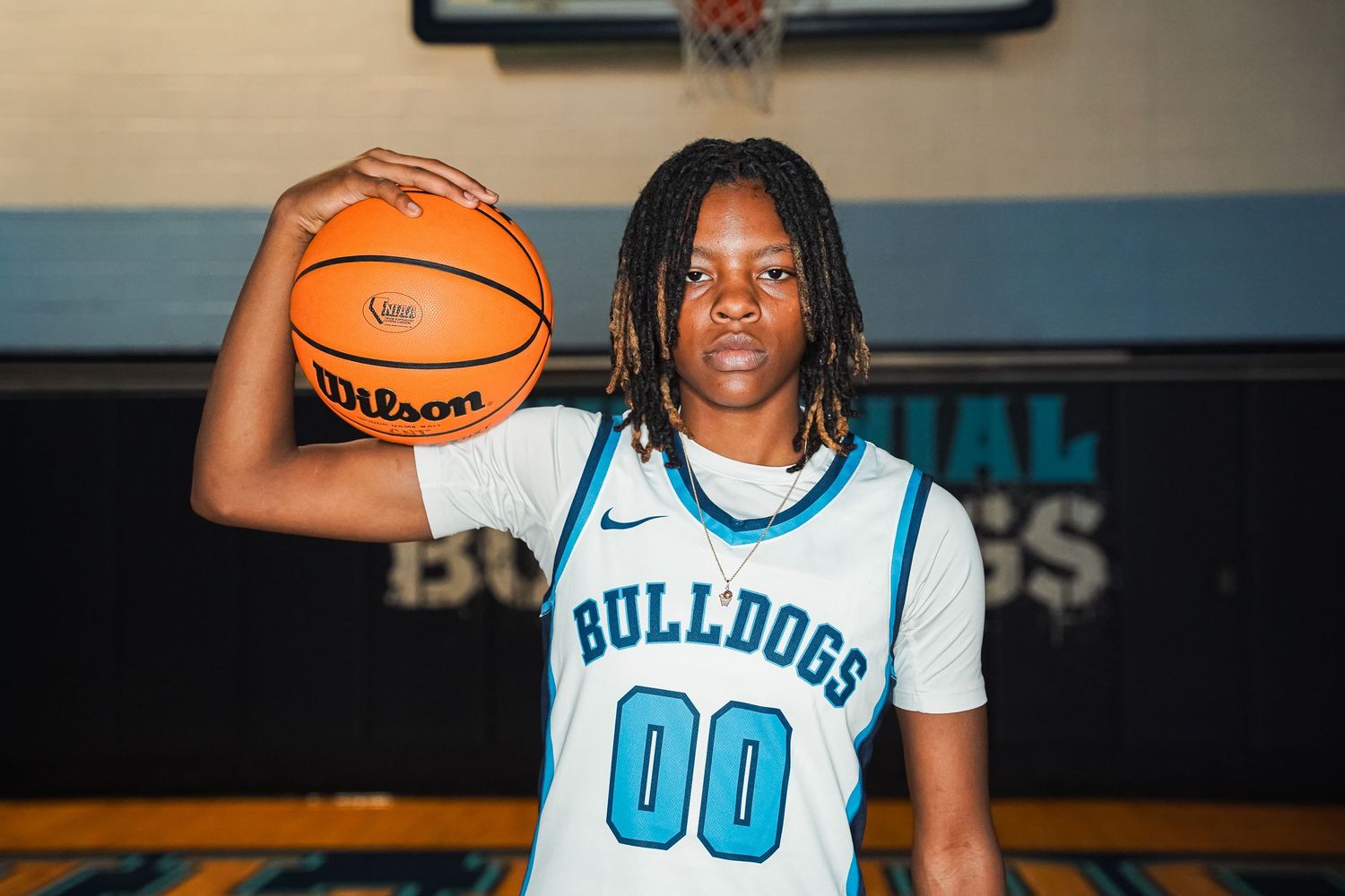 Basketball player in white Bulldogs jersey number 00 holds basketball in front of team logo.