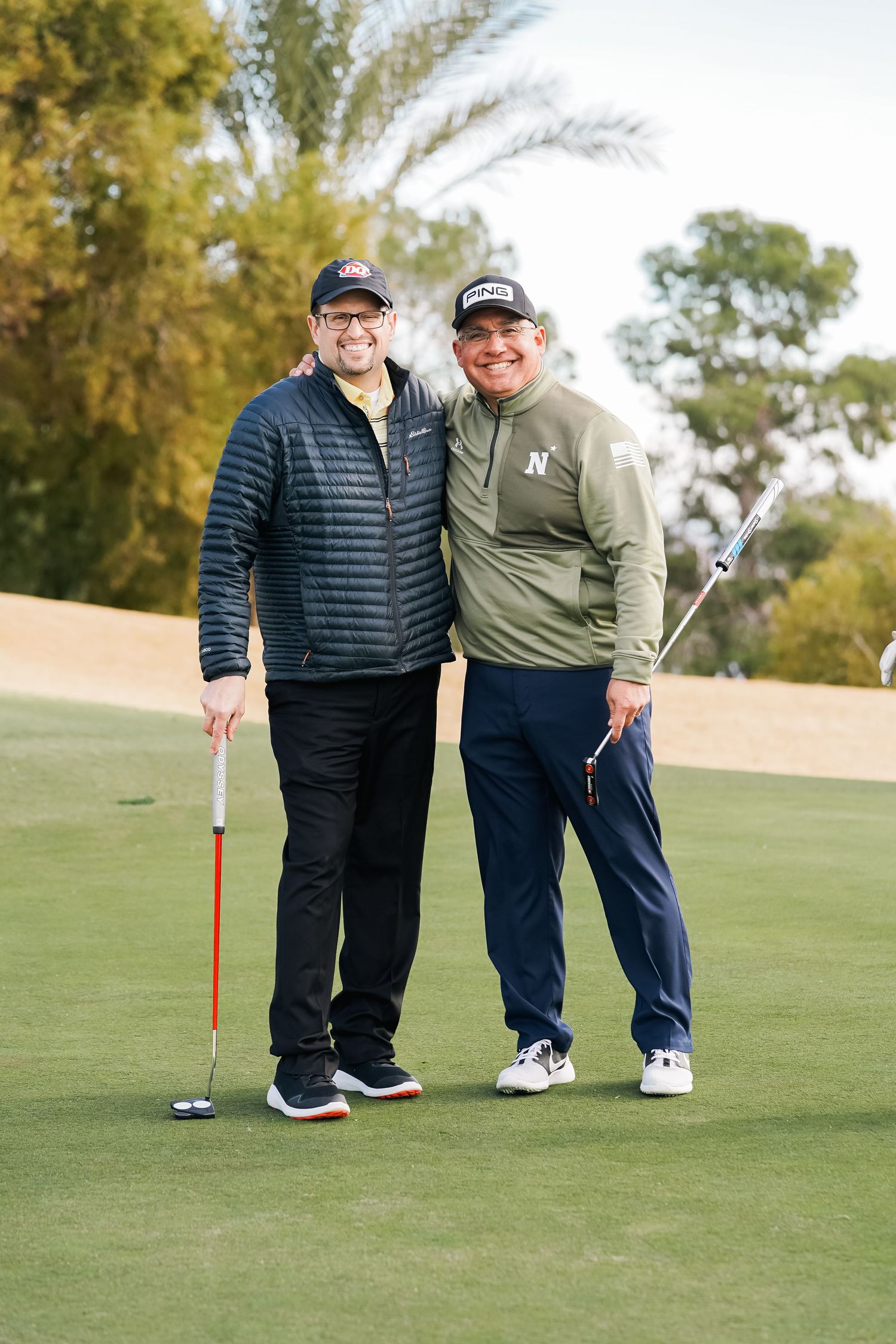 Two golfers posing with their clubs on the golf course.