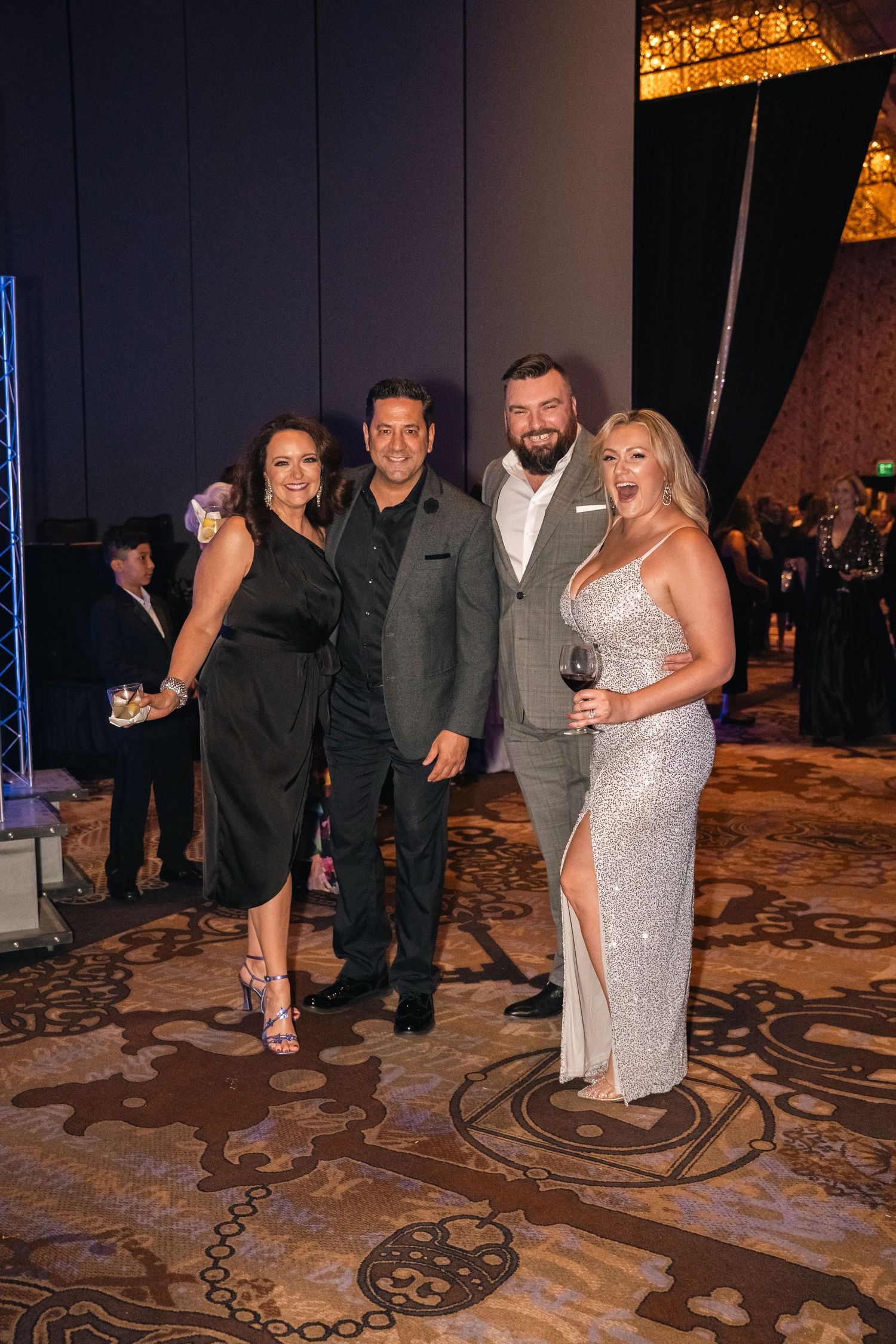 Group poses on patterned carpet at formal evening gala event.