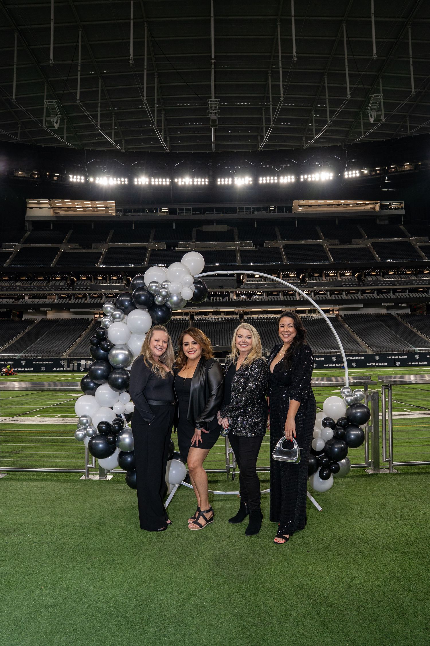 Group photo with black and white balloon arch on a football field inside stadium.