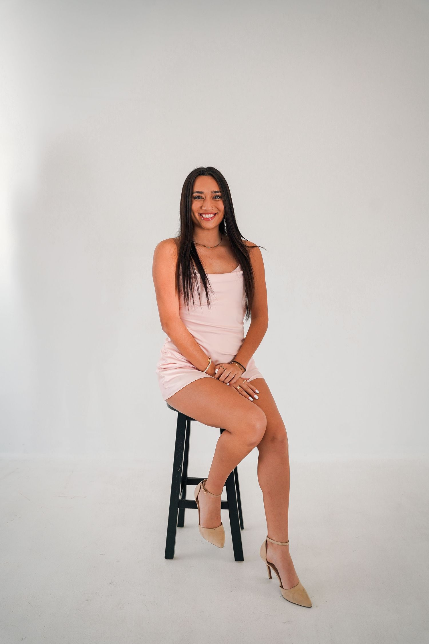 Woman in pink dress sitting on black chair in studio setting with white background.