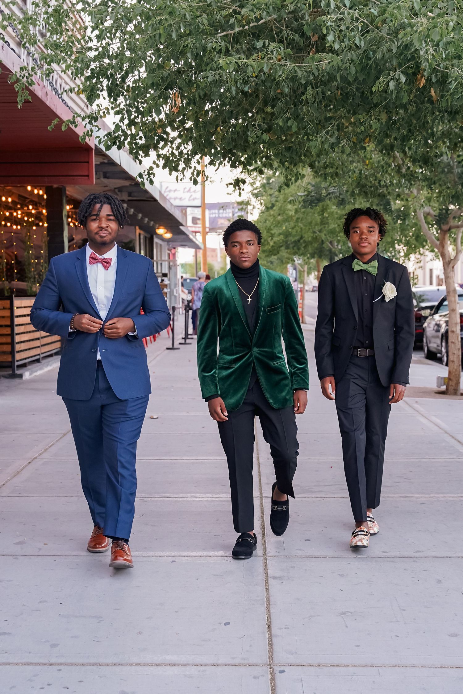 Three well-dressed people walking on sidewalk, with one wearing emerald velvet suit and others in classic suits.