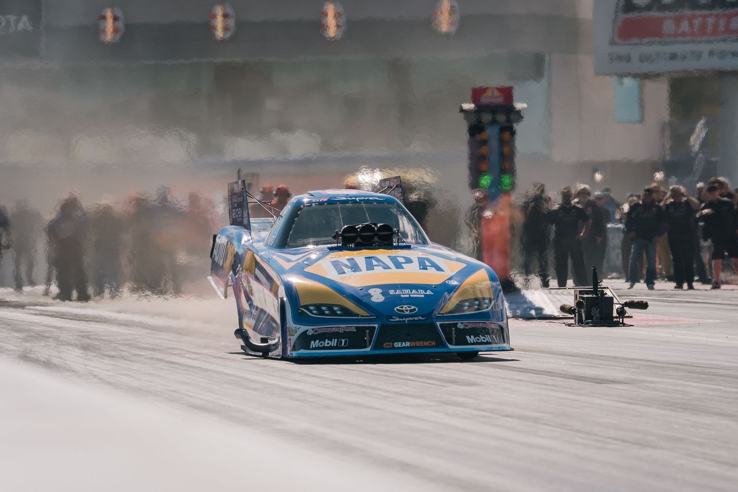Racing car speeding down a smoky drag strip during a competitive event.